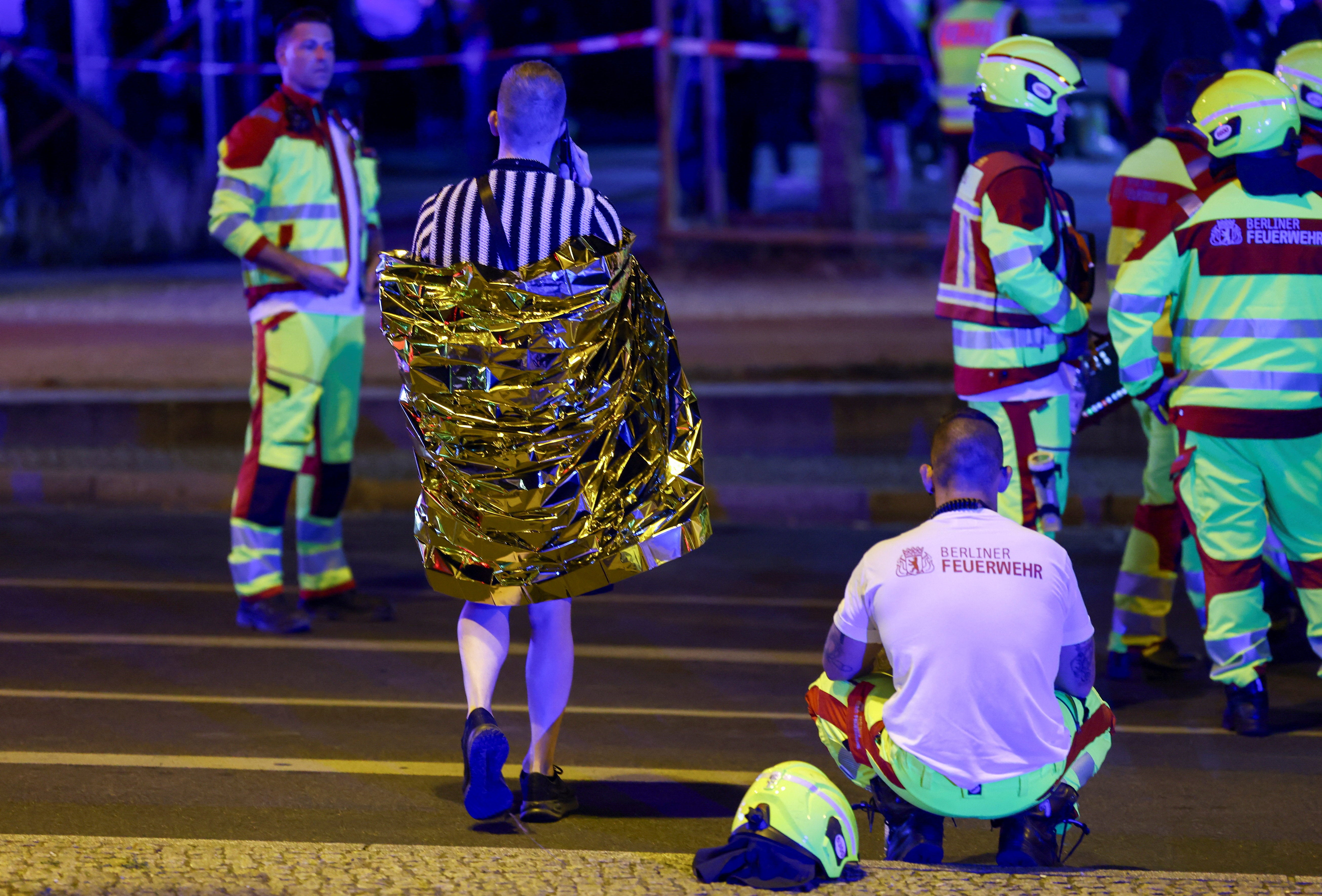 A person wrapped in a thermal blanket walks as emergency responders work at the site after the annual Berlin's Christopher Street Day Pride parade