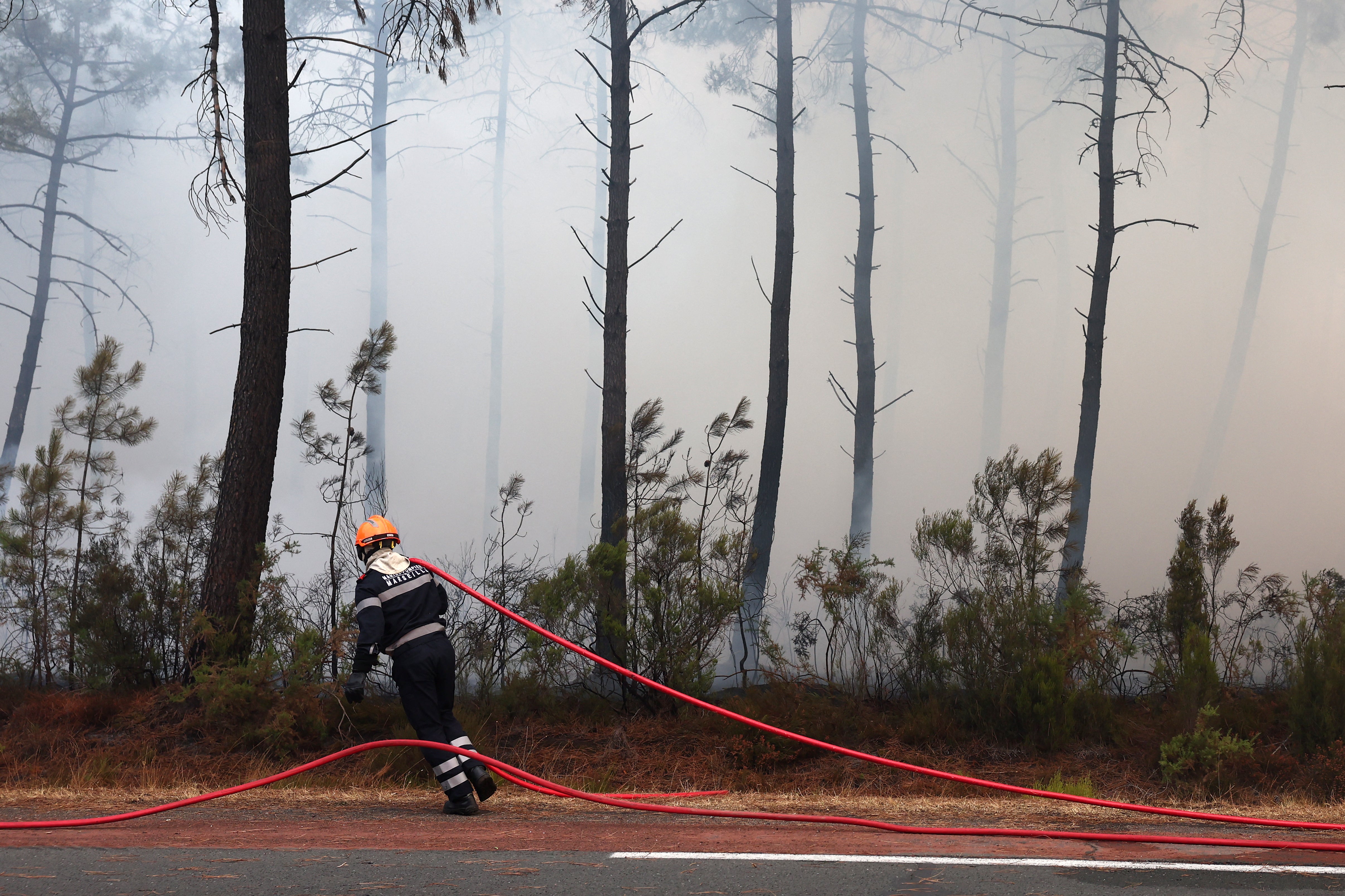 A firefighter from Marseille pulls a hose amid smoke in Ares on July 26, 2026 as a wildfire has been ravaging the forest north of the Arcachon Basin (Gironde) since July 22. The fire that has engulfed the area around the Arcachon Basin and is now threatening the outskirts of the Bordeaux metropolitan area has destroyed 42,000 hectares of 