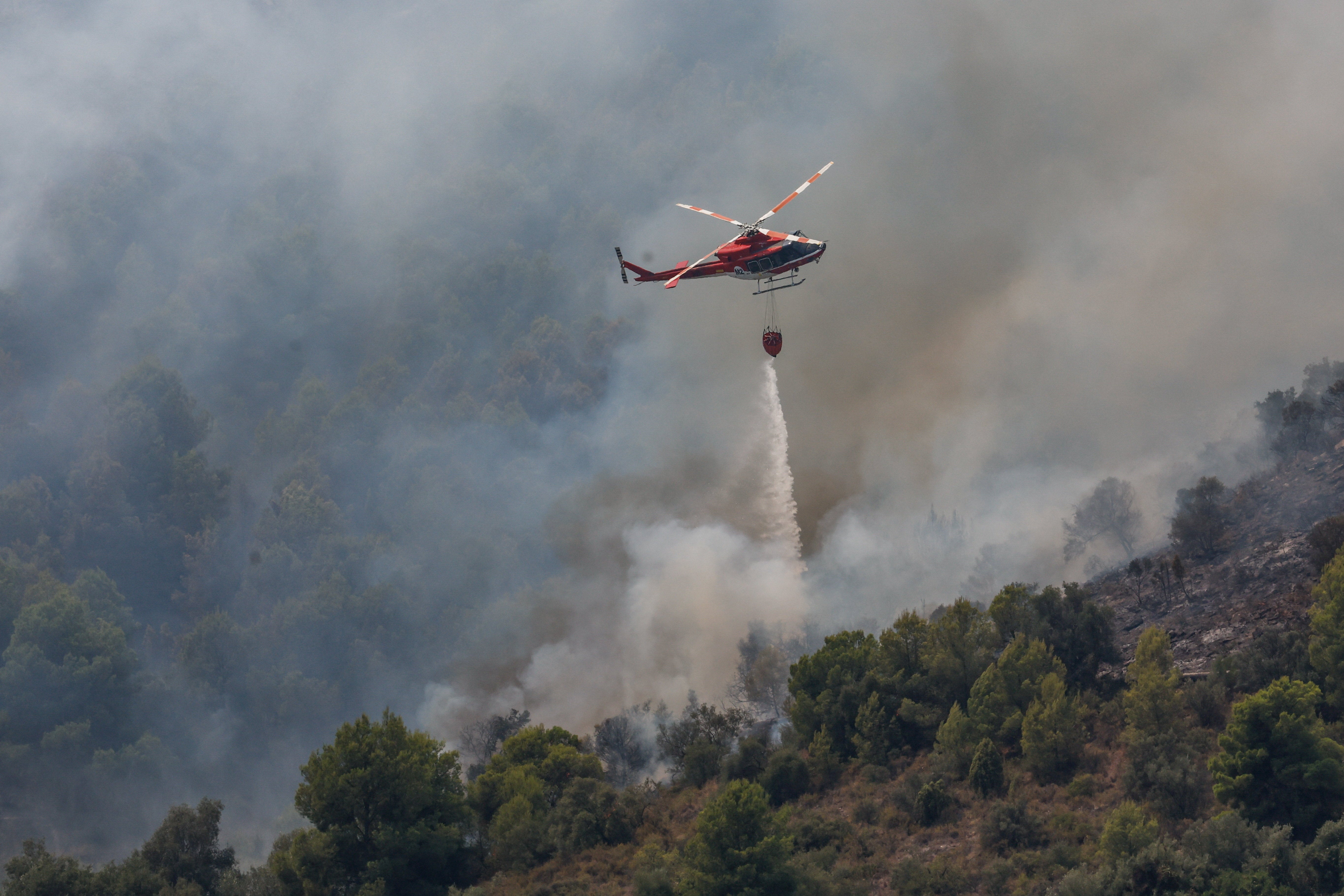 A helicopter makes a drop as smoke rises from a wildfire in Betxi, Spain, July 26, 2026. (Reuters)
