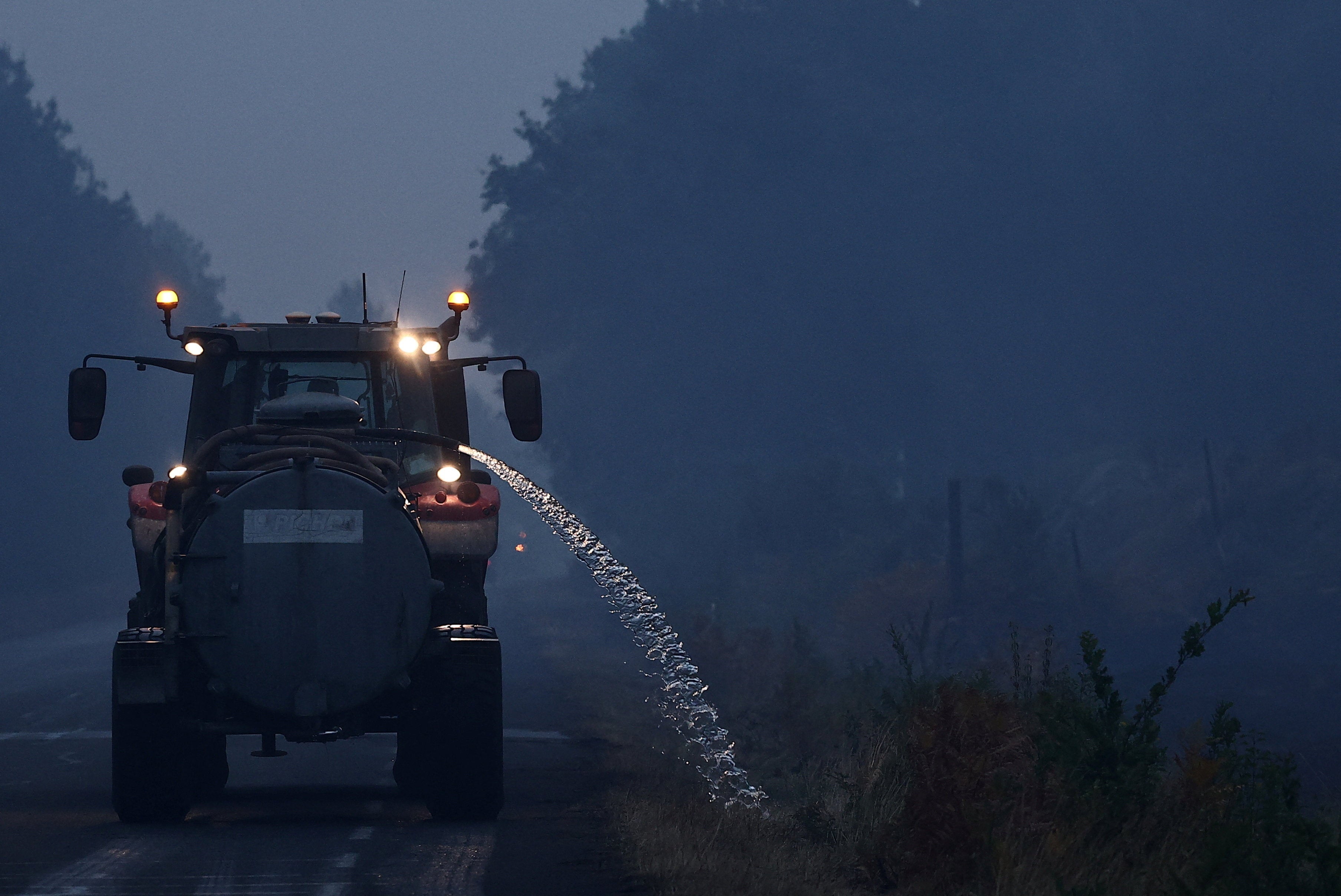 An agricultural worker drives a tractor while wetting roadside vegetation as a preventive measure to help stop wildfires from spreading, as wildfires rage across the Gironde region amid worsening drought conditions following a heatwave and water shortages across much of France, near Sainte-Helene, France