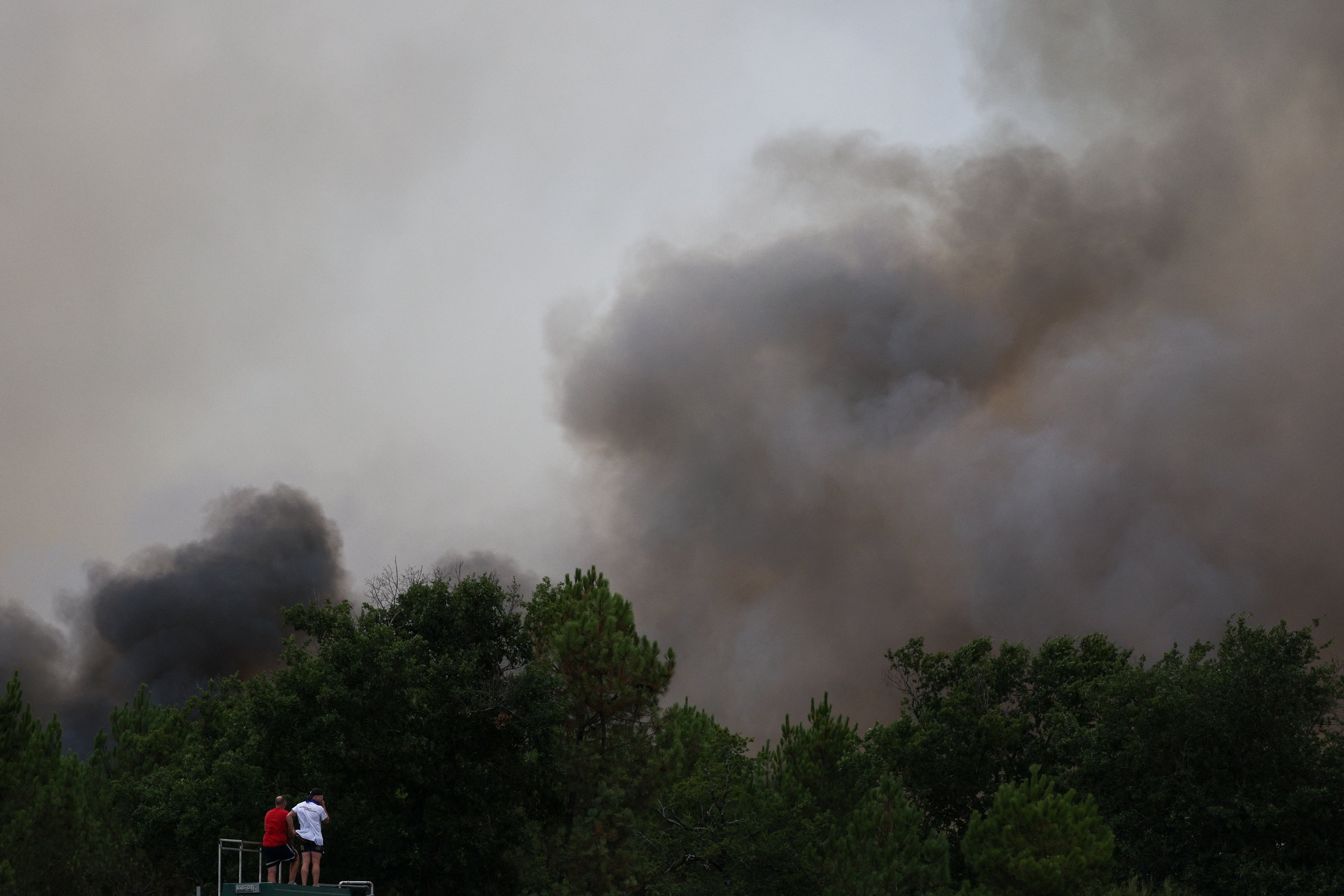 People watch a wildfire from atop a vehicle, amid worsening drought conditions following a heatwave and water shortages across much of the country, in Marcheprime, France