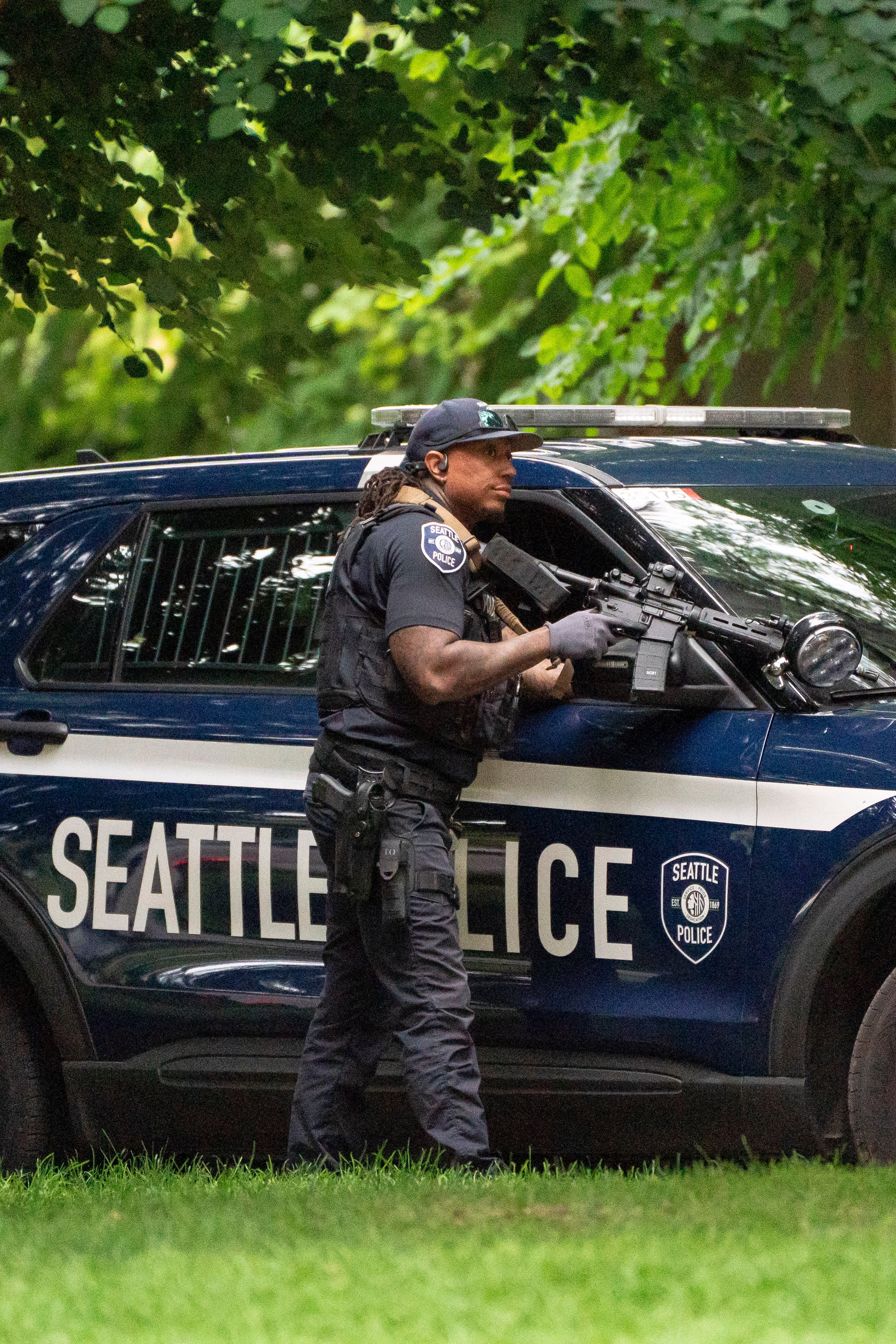 A police officer holds a weapon behind a police vehicle after a mass shooting at the Bite of Seattle food festival on 26 July 2026 in Seattle, Washington