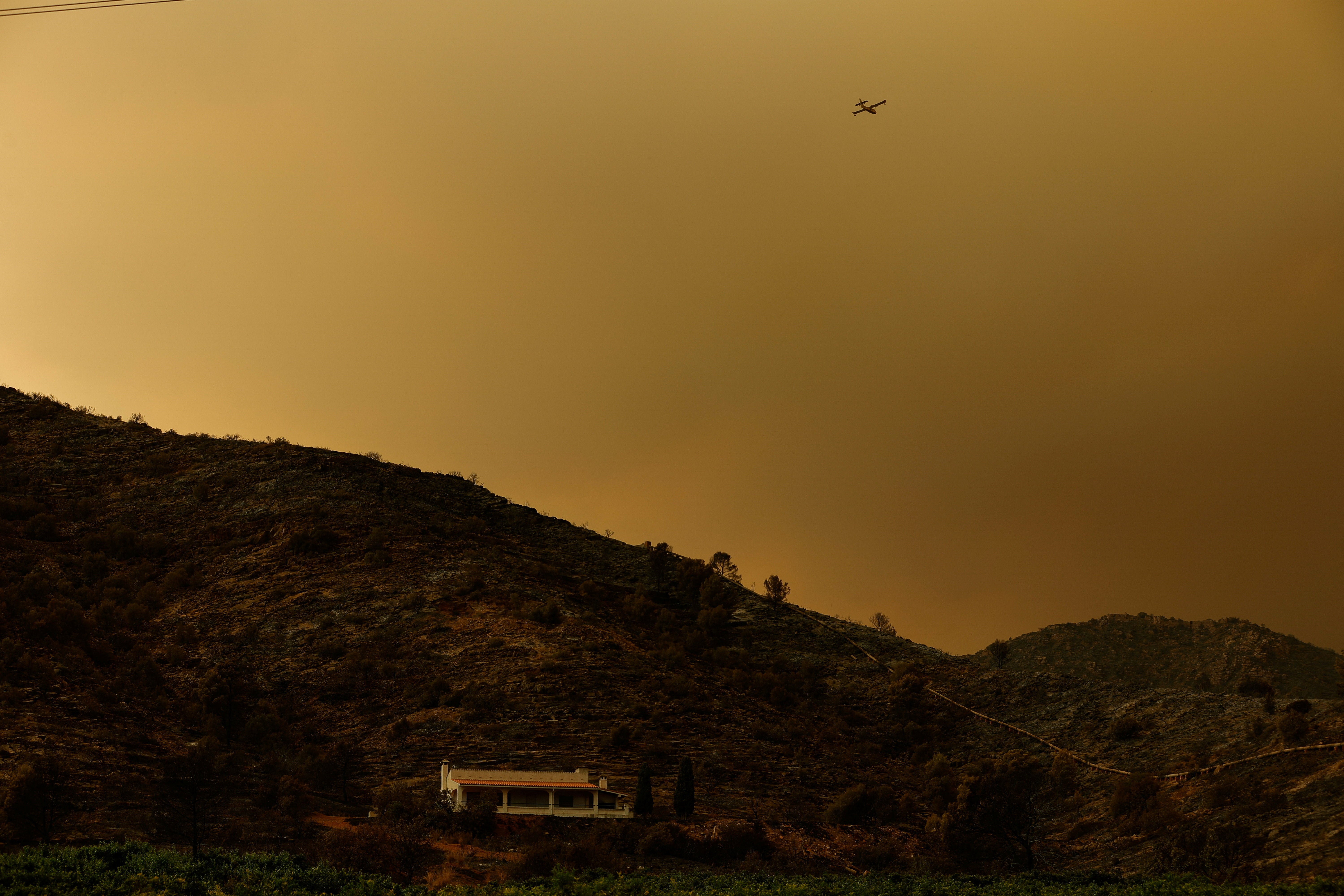 A plane flies as smoke rises from a wildfire in La Vall d'Uixo, Castellon, Spain (Reuters)