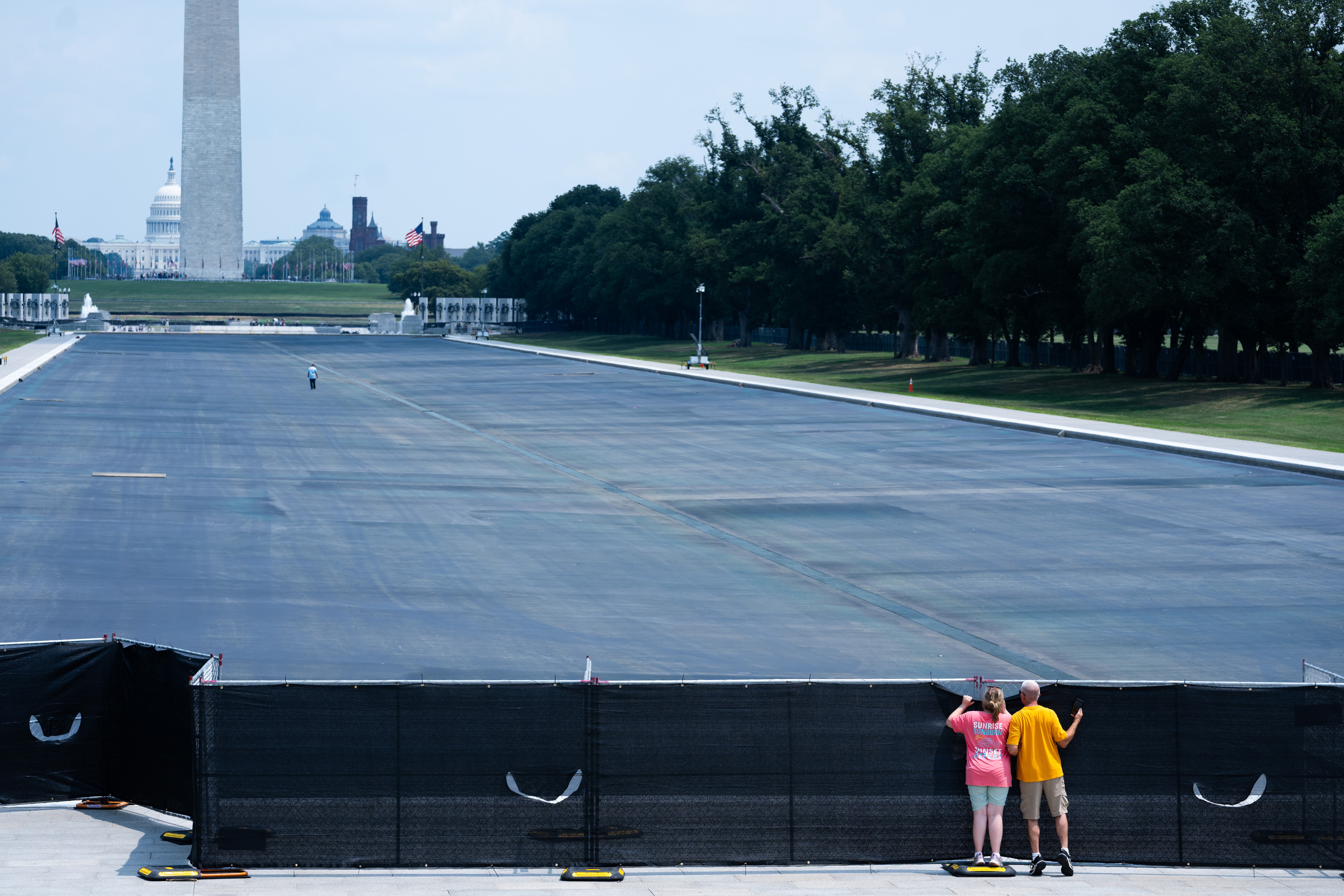 Individuals peek over the fence to see the drained Lincoln Memorial Reflecting Pool,, Monday, July 27