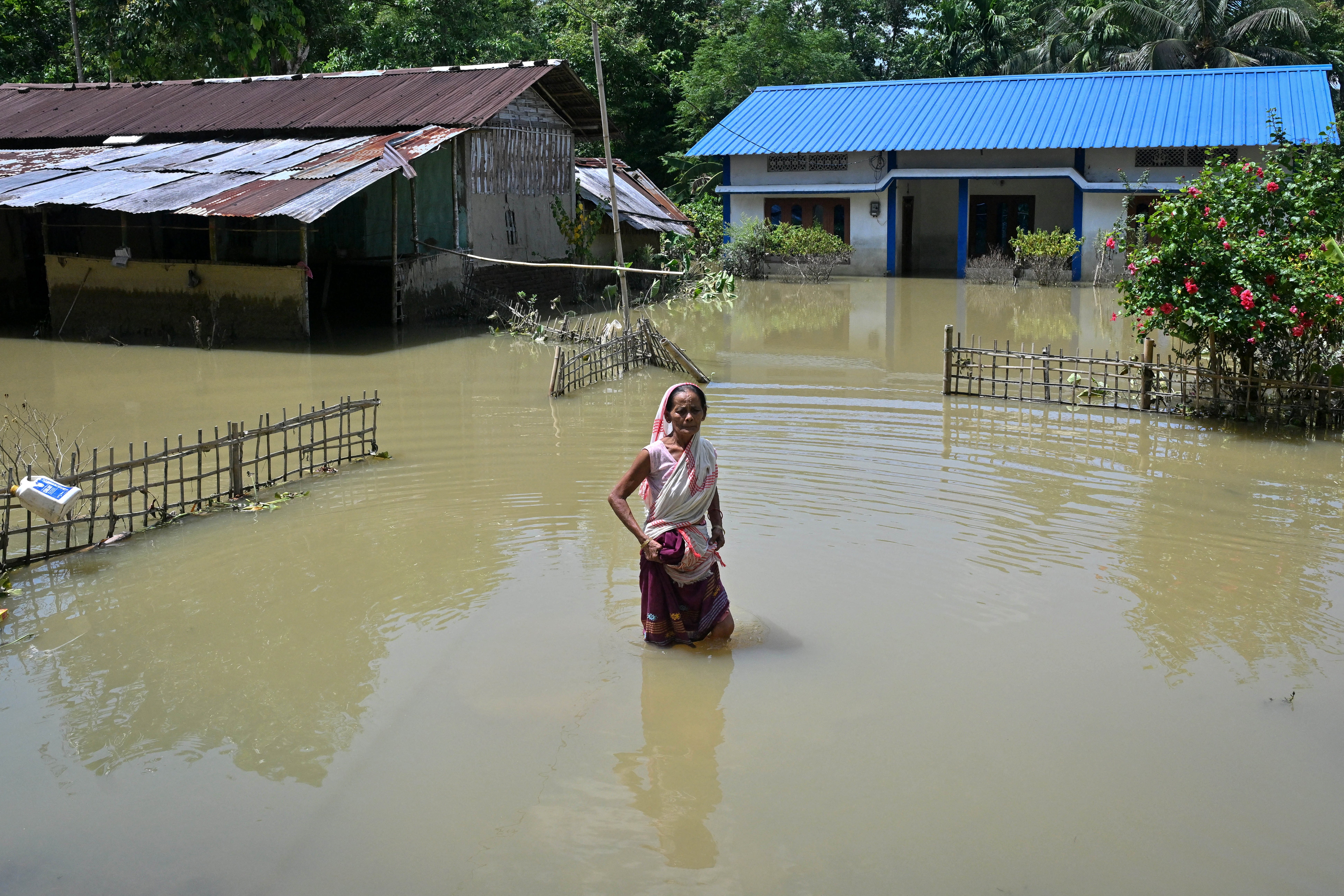 An elderly woman wades through floodwaters near her partially submerged house following heavy monsoon rains at a village in Assam's Sivasagar district on 27 July 2026 (AFP/Getty)