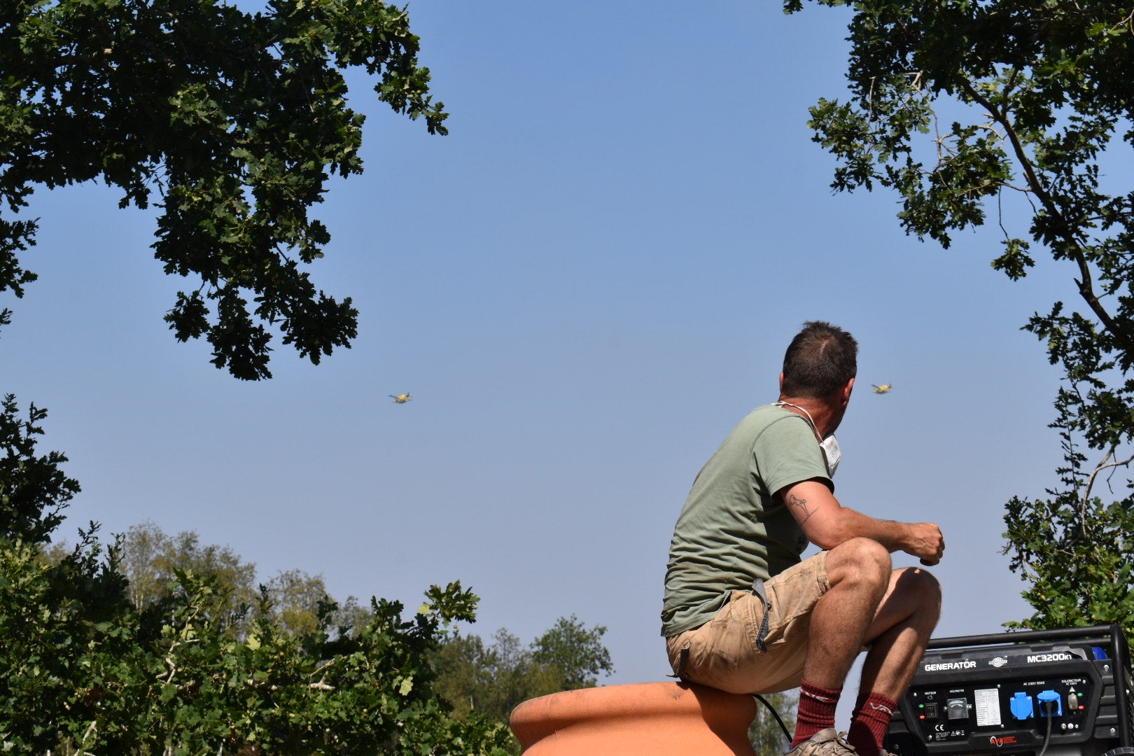 A volunteer on top of a truck watches as Canadair water bombers pass overhead