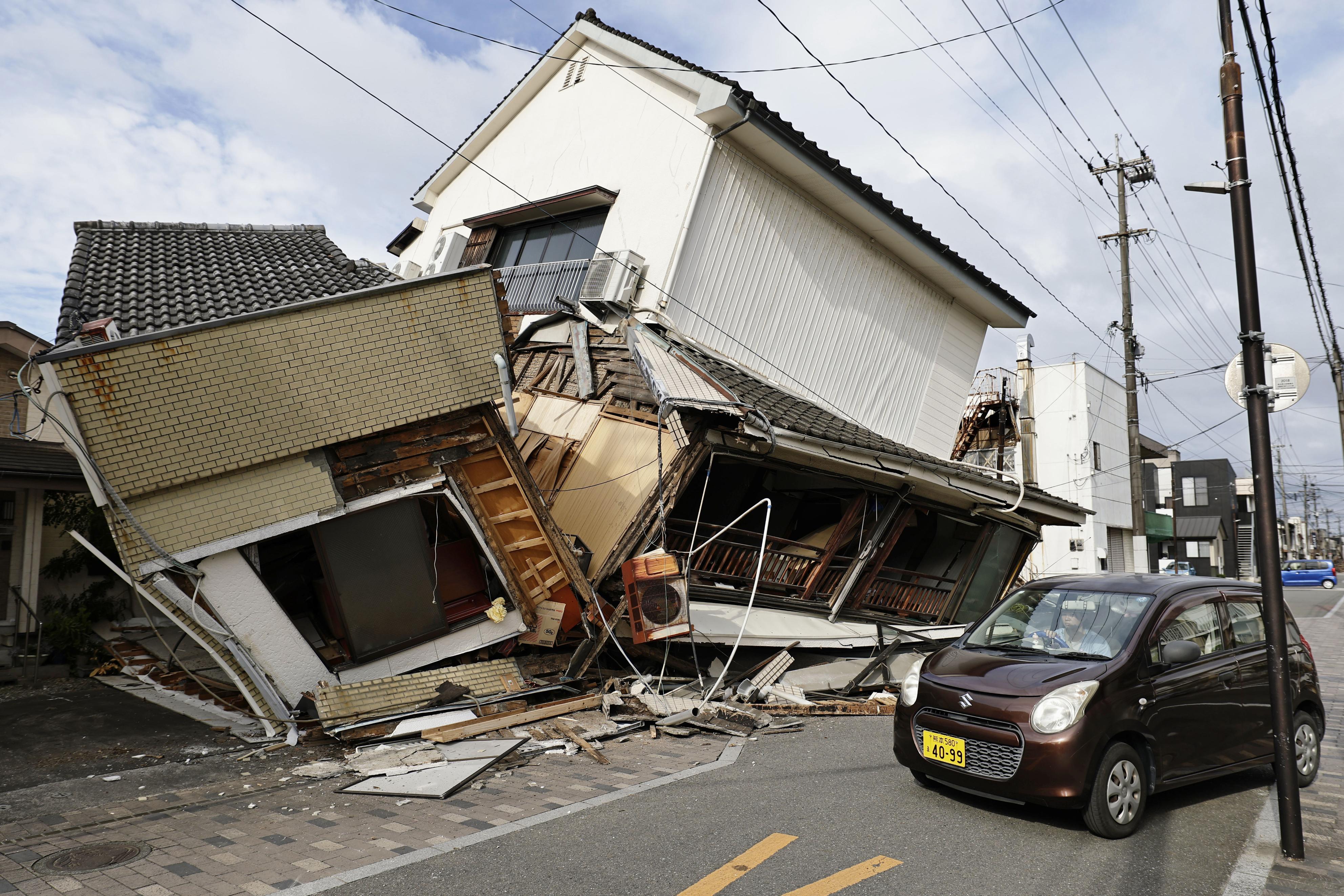 A vehicle passes by collapsed houses after an earthquake in Yatsushiro, Kumamoto prefecture (AP)