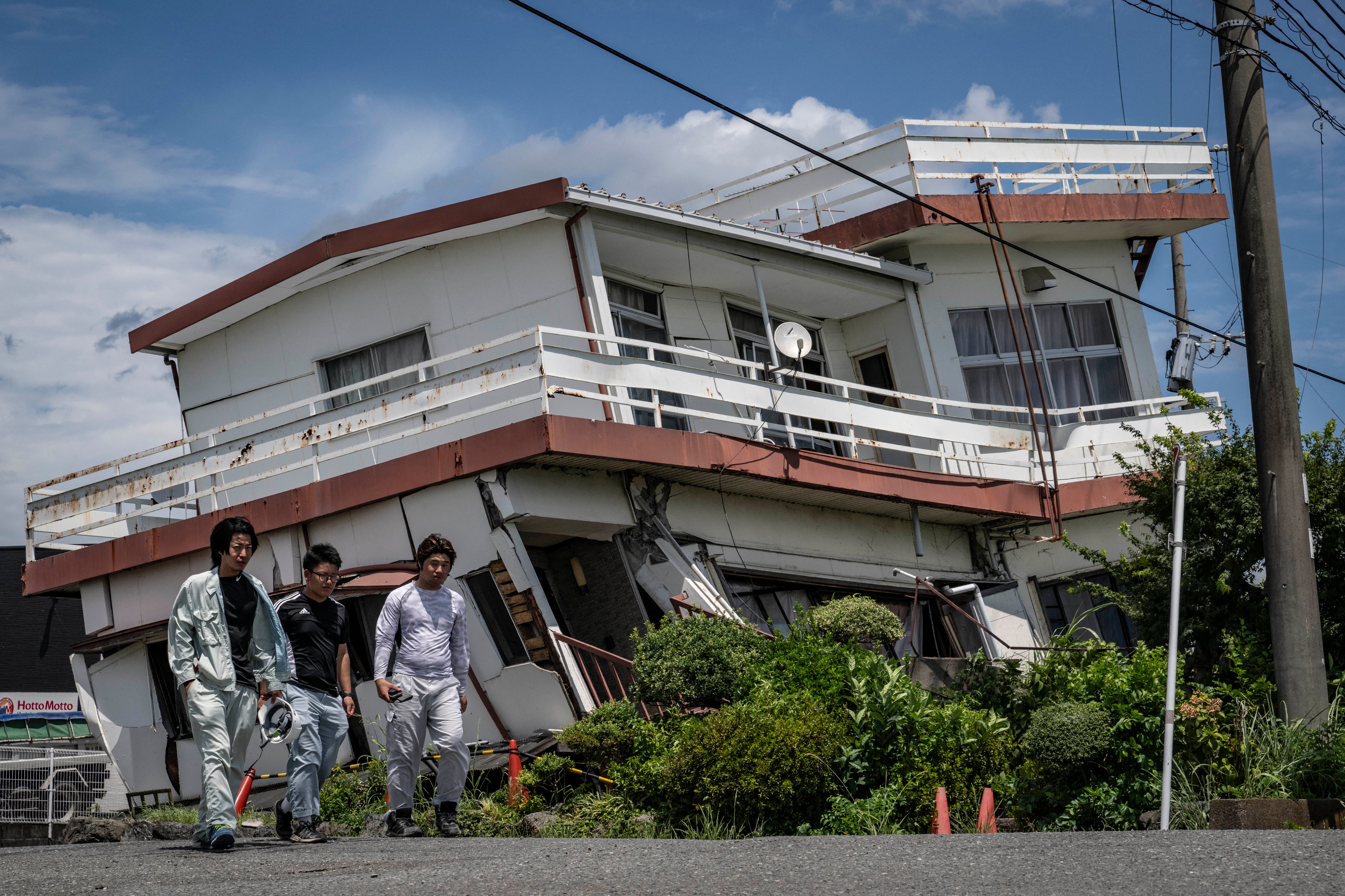 Workers walk past a damaged house and partially collapsed in Yatsushiro, Kumamoto prefecture on July 29, 2026, after an earthquake struck southwestern Japan the previous day (AFP/Getty)