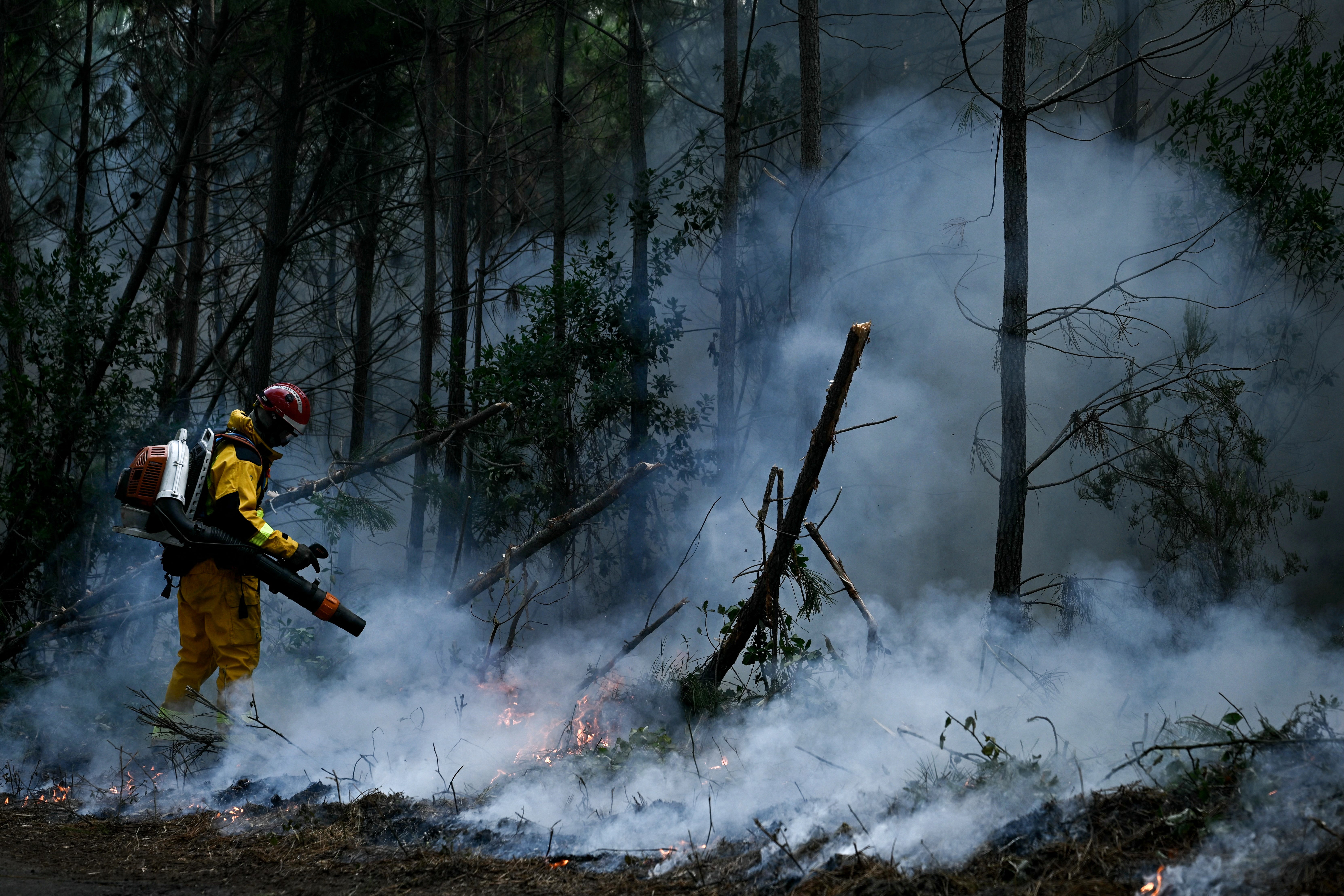 A firefighter uses a backpack blower to clear vegetation and create a firebreak during a controlled fire operation in a forest in Le Porge, north of the Arcachon Basin