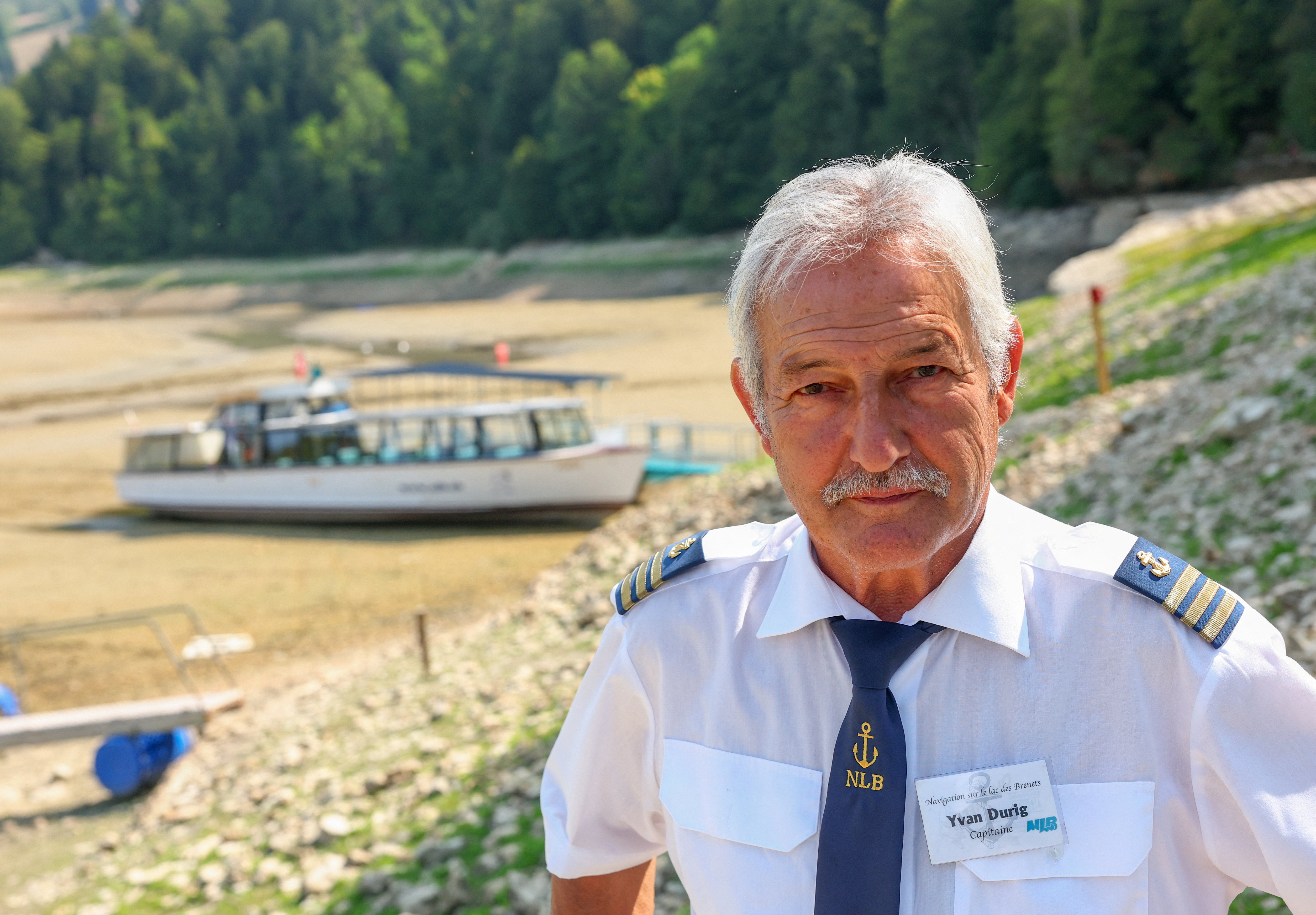Yvan Durig, owner of the Societe de Navigation des Brenets, poses in front of a moored boat on the nearly empty Lake Brenet, as drought conditions affecting the Doubs River lower water levels at the Swiss-French border in Les Brenets, Switzerland, July 30, 2026. REUTERS/Denis Balibouse