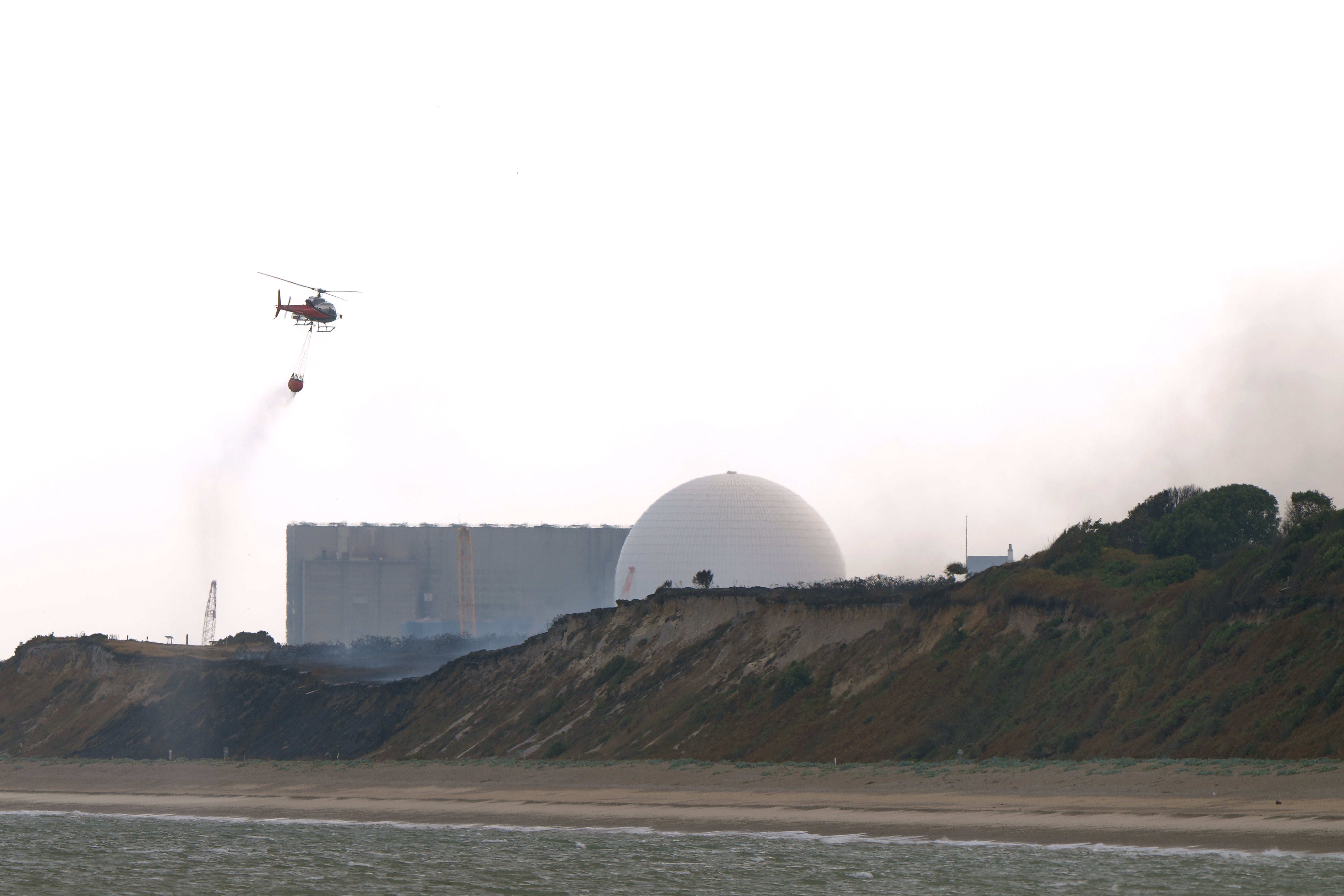 A helicopter flies water collected from the sea to drop on the wildfire at Dunwich Heath, near Leiston, close to the Sizewell B nuclear power station (Joe Giddens/PA) (PA Wire)