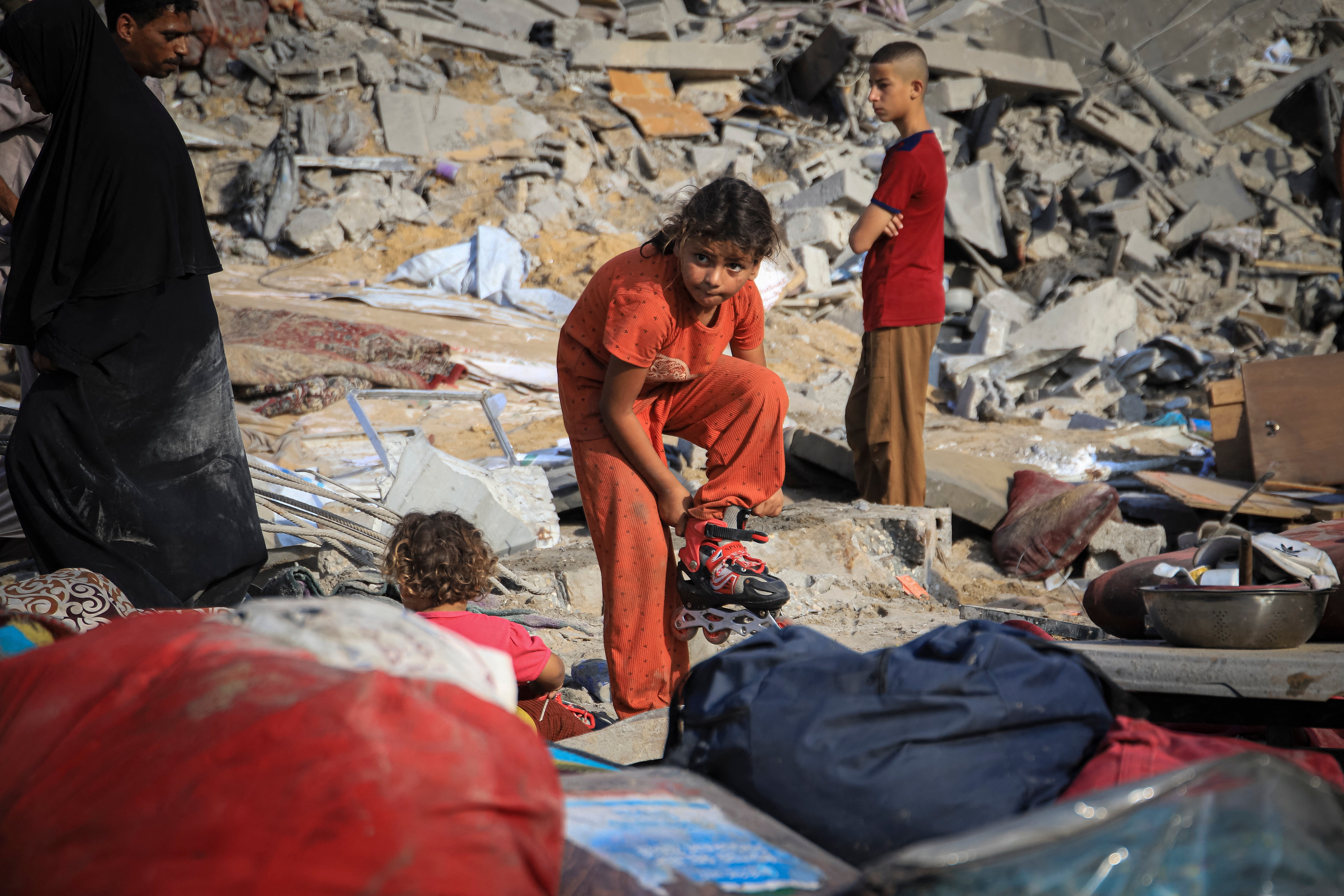 Palestinian children search among clothing and household belongings scattered across the rubble after an Israeli airstrike in the Al-Nasr