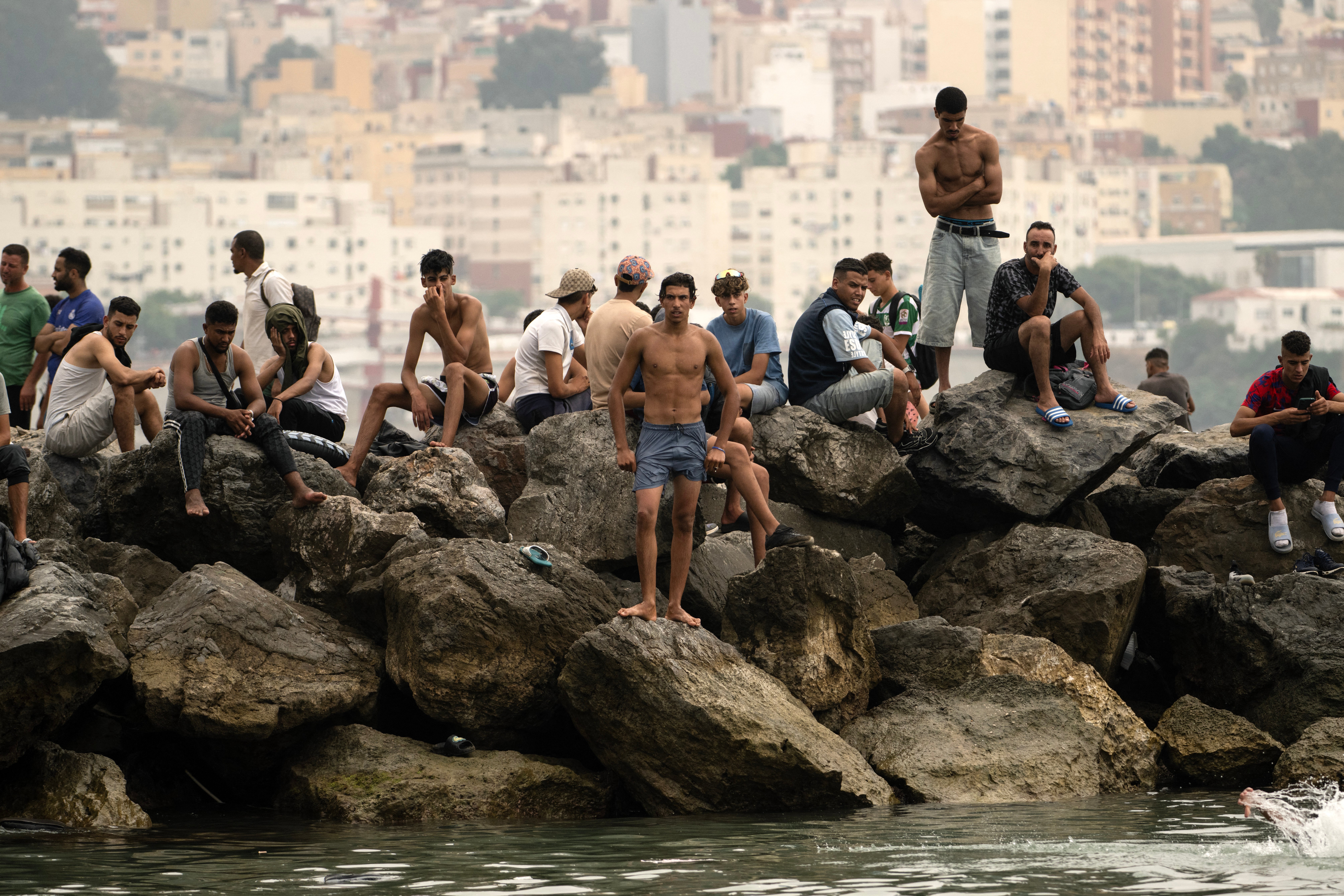 Migrants sit on rocks after swimming through the waters close to the border with Morocco