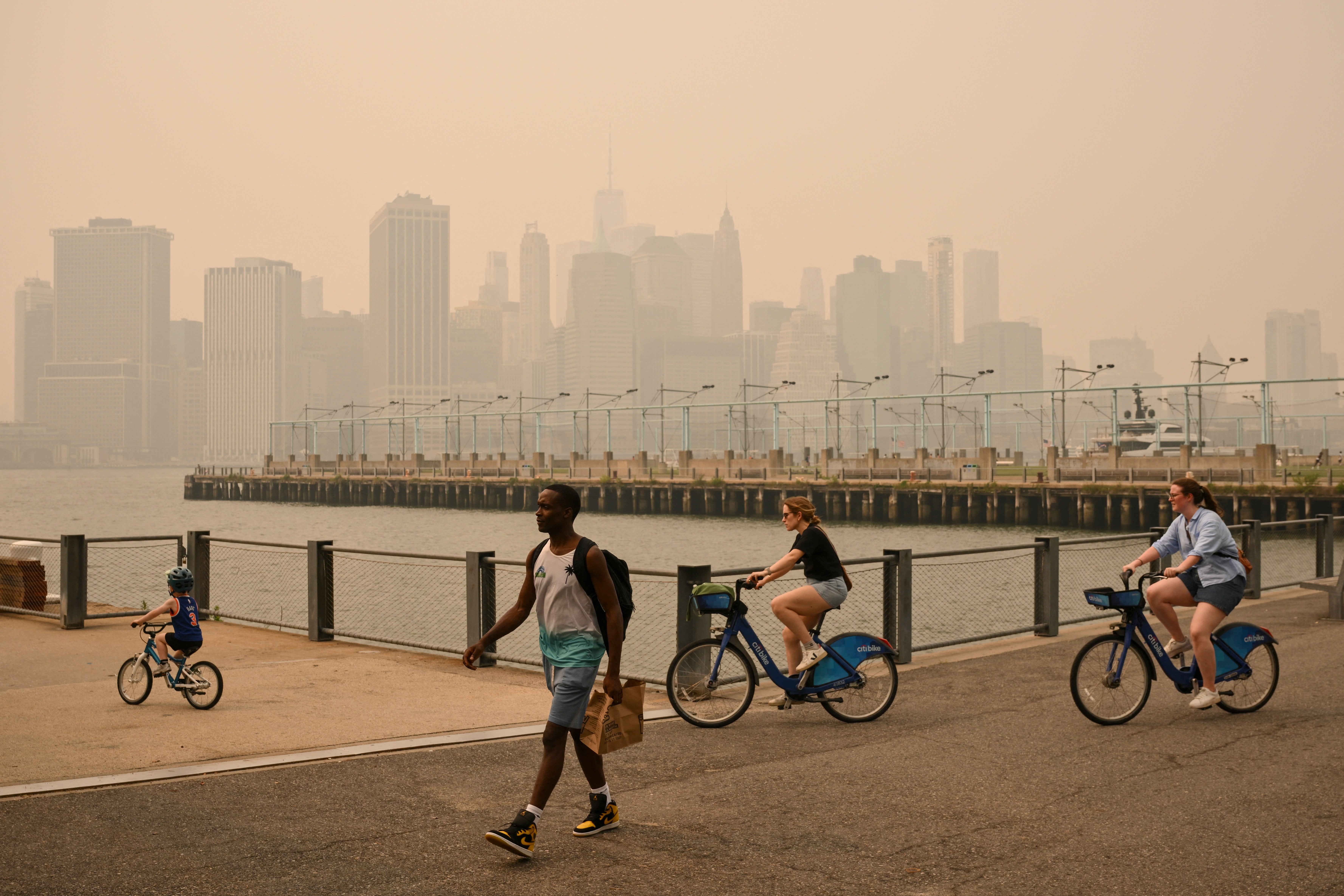 People walk and bike in New York City earlier this month as dangerous Canadian wildfire smoke fills the skies. Wildfire smoke has been linked to developing cancer