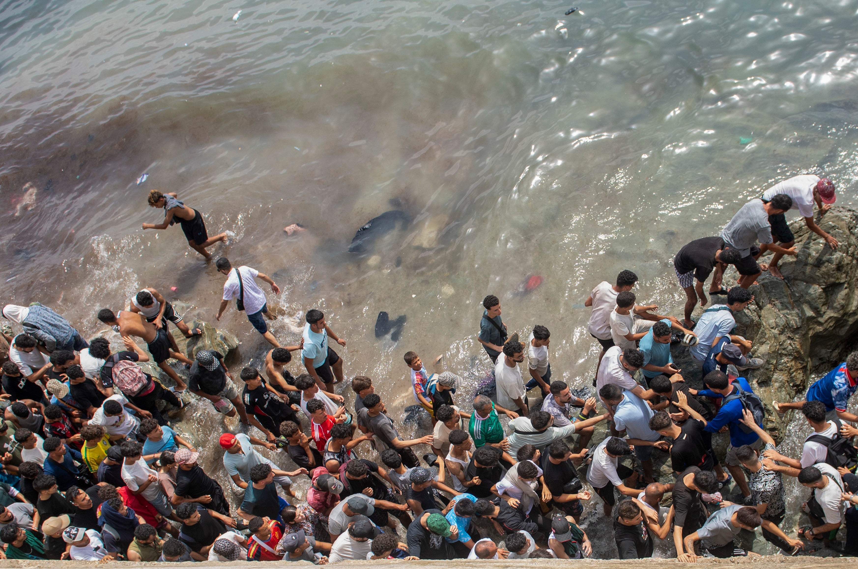 People walk on a beach as they attempt to cross from the Moroccan northern town of Fnideq to the Spanish enclave of Ceuta