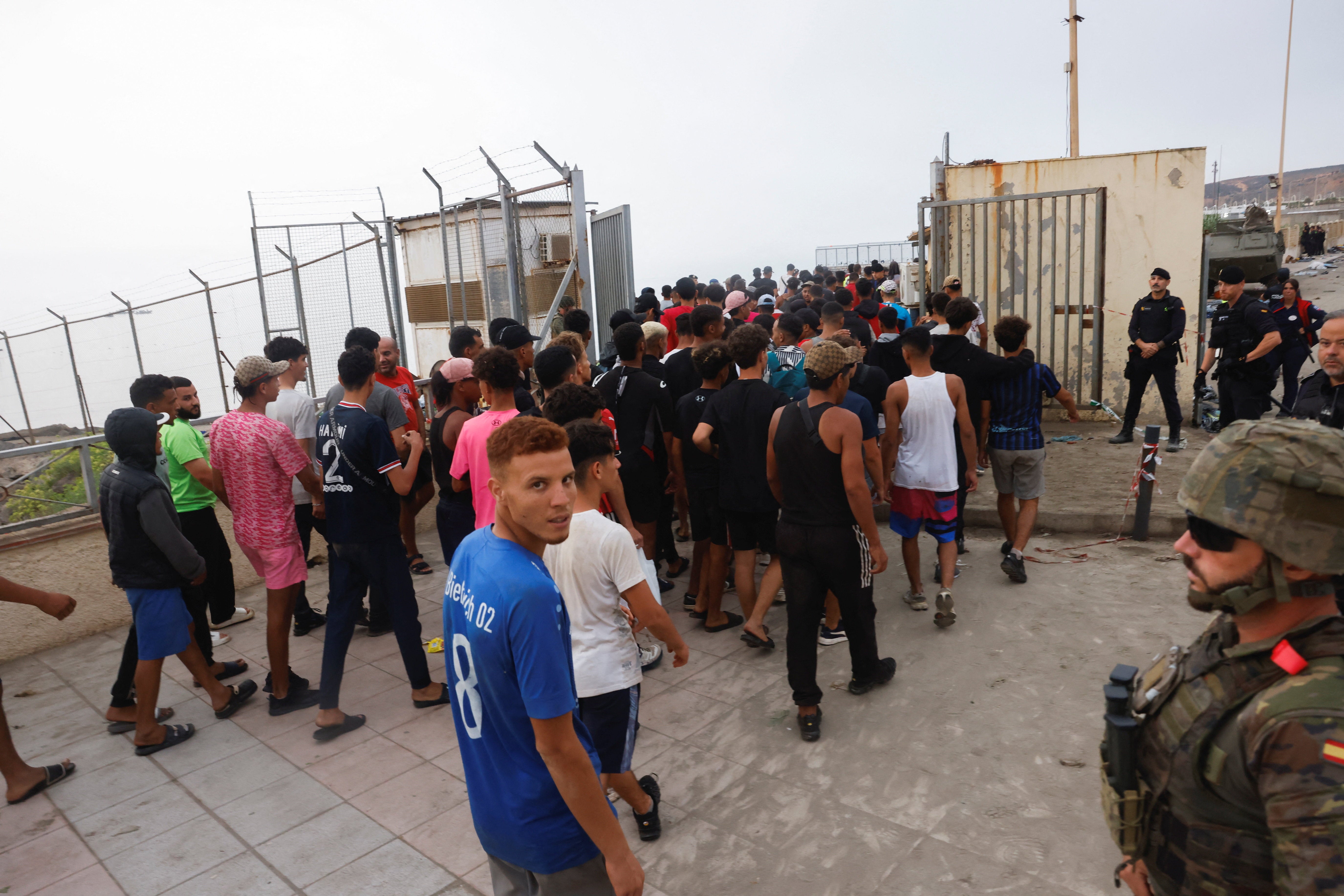 Police officers and a Spanish soldier stand guard as a big group of migrants are escorted near the border