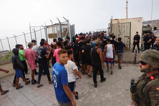 Police officers and a Spanish soldier stand guard as a big group of migrants are escorted near the border