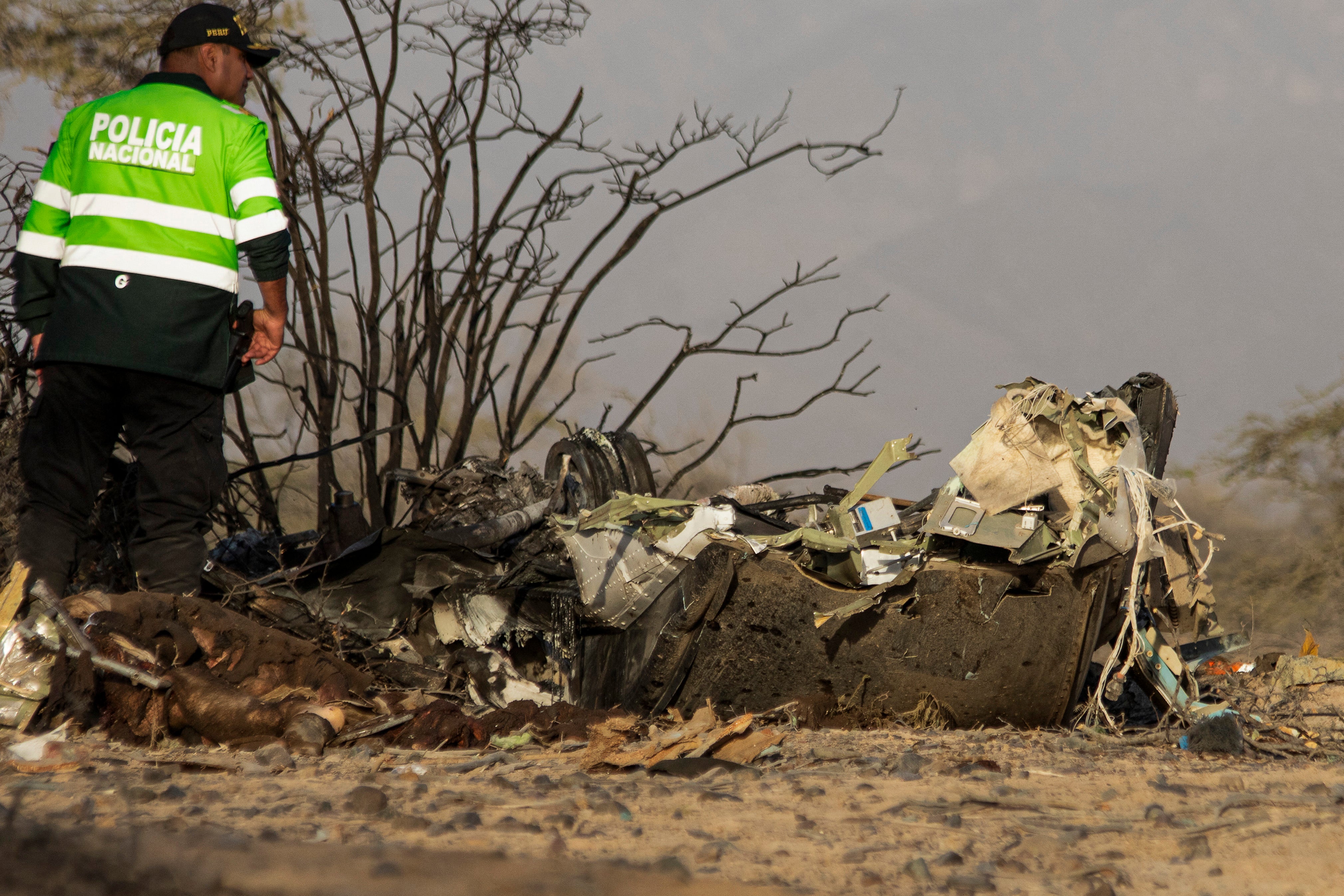 A police officer stands alongside the wreckage of the small plane involved in a fatal accident that claimed the lives of its 13 occupants in the Vista Alegre district, Nazca