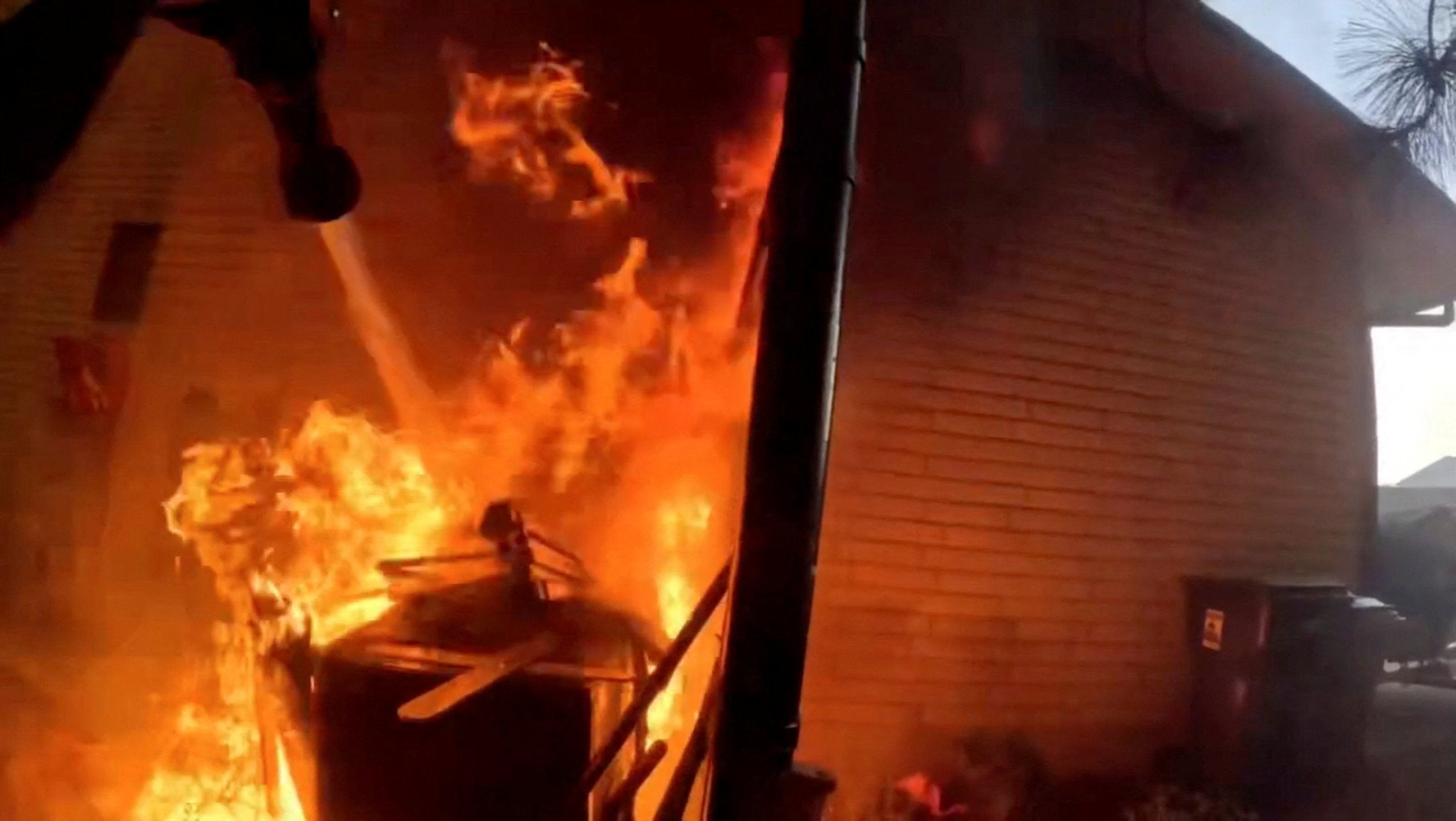 A firefighter works to put out a fire at a home as a wildfire burns in Spokane County (Spokane County Fire District)