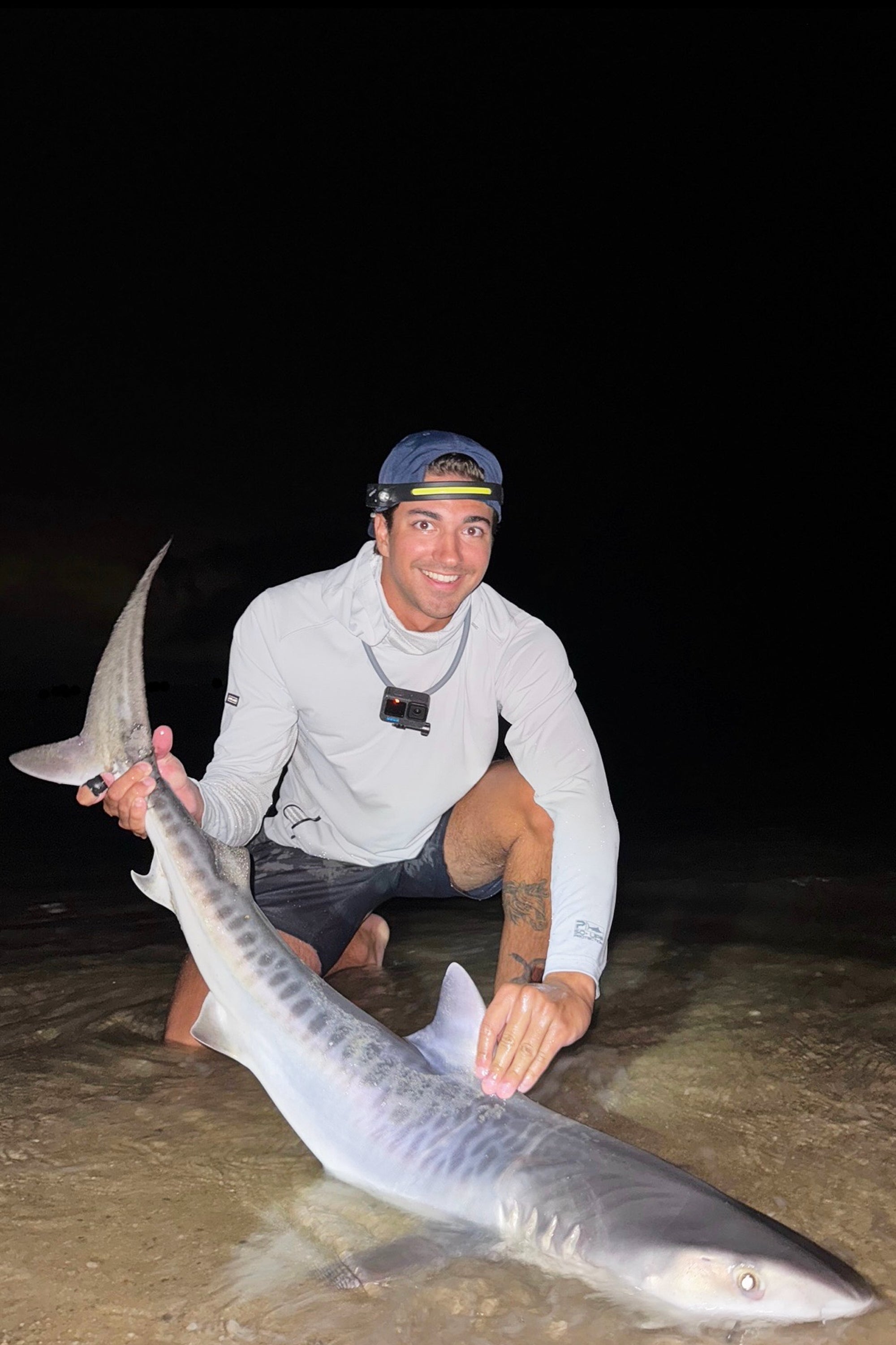 This photo provided by Nelson Rouette shows his brother, Nate Rouette, holding a young tiger shark that they caught off Falmouth Mass., July 23, 2026. (Nelson Rouette via AP)