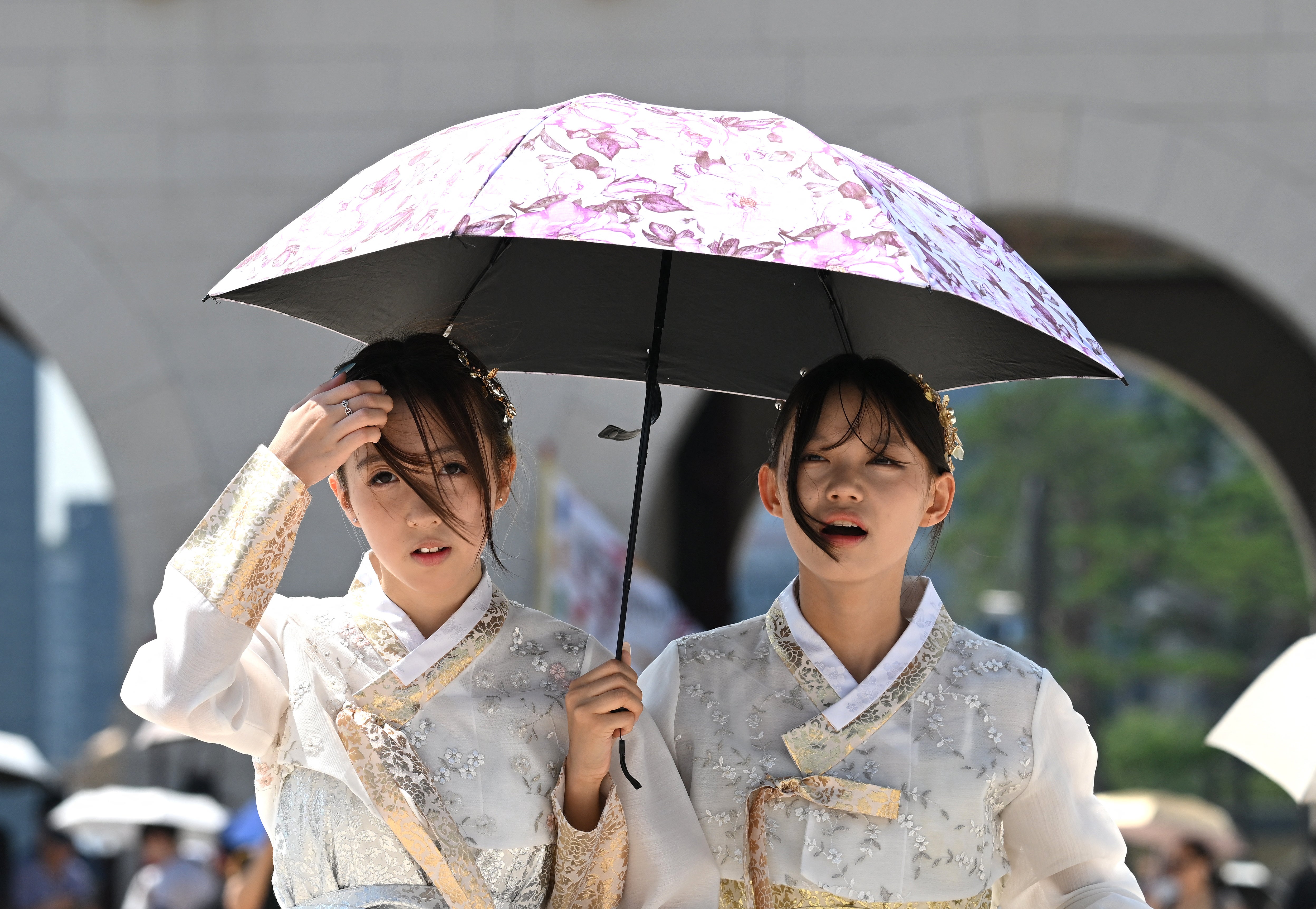 Tourists wearing traditional Hanbok dresses use a parasol to shield from the sun at the Gyeongbokgung Palace in Seoul