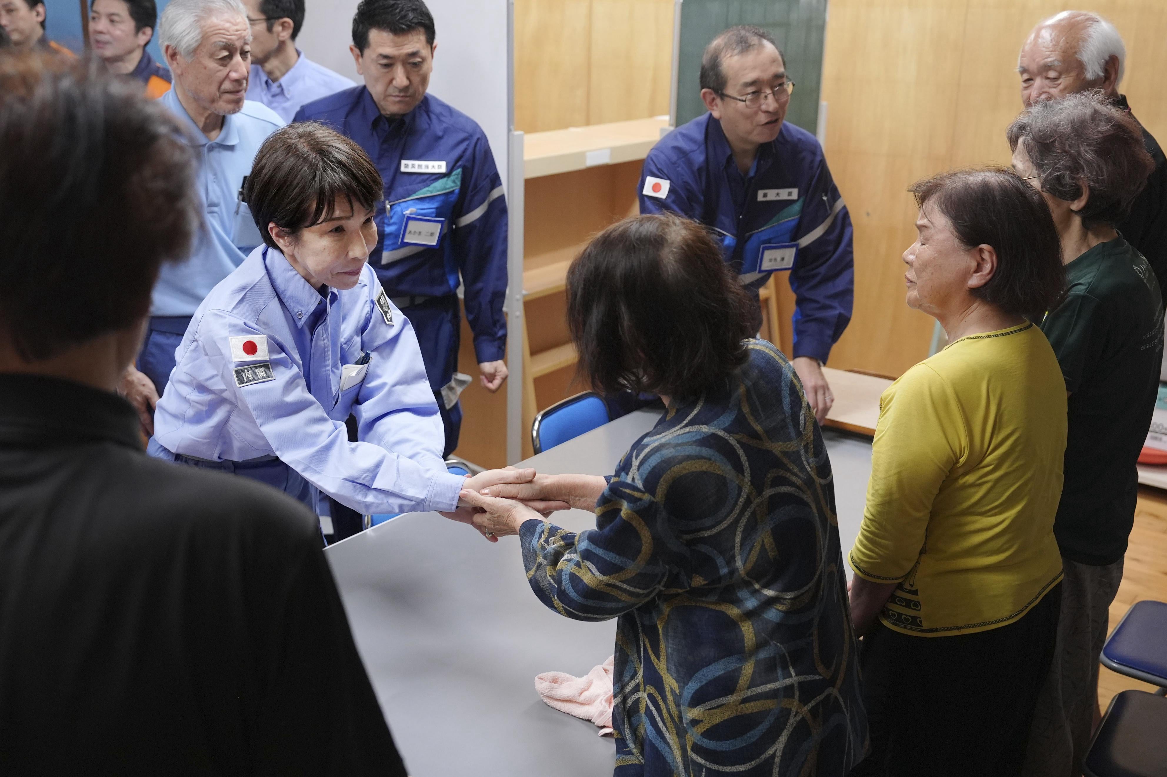 Japan's Prime Minister Sanae Takaichi, center left, greets evacuees as she visits an evacuation center in Hikawa, southern Japan