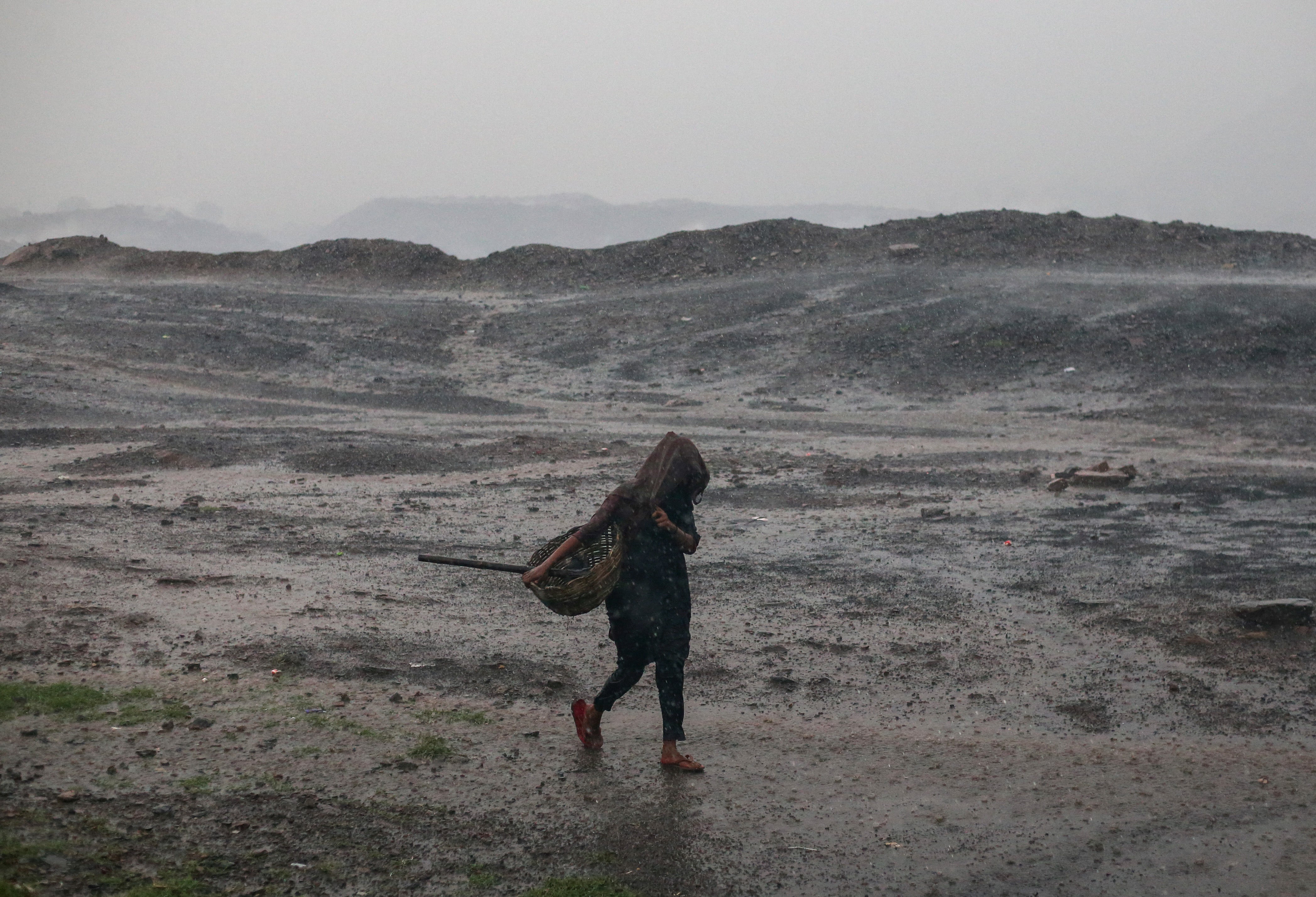 A woman carrying a trug of coal crosses an underground coal fire land during heavy rains in Jharkhand (Getty)
