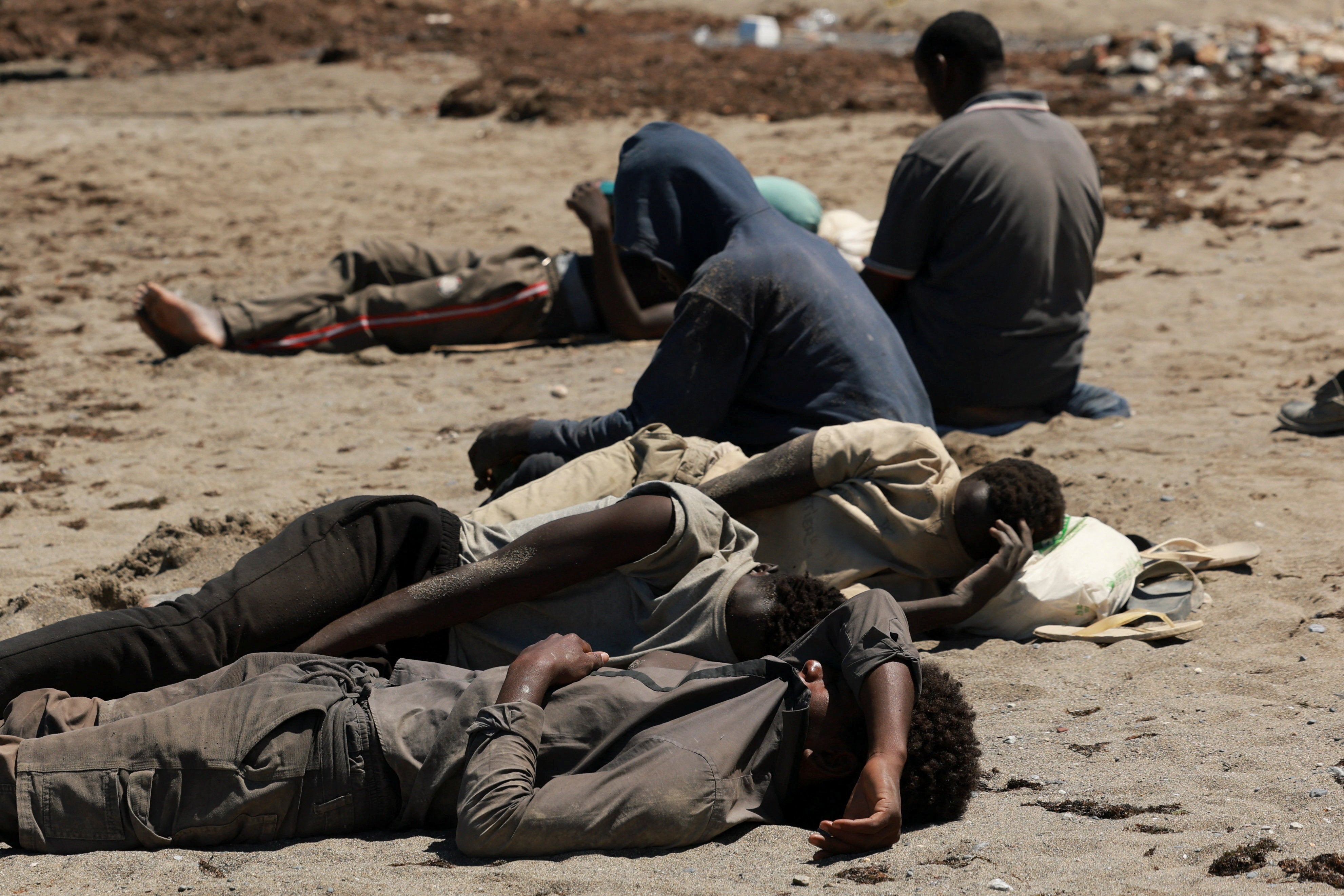Migrants rest while waiting on a beach