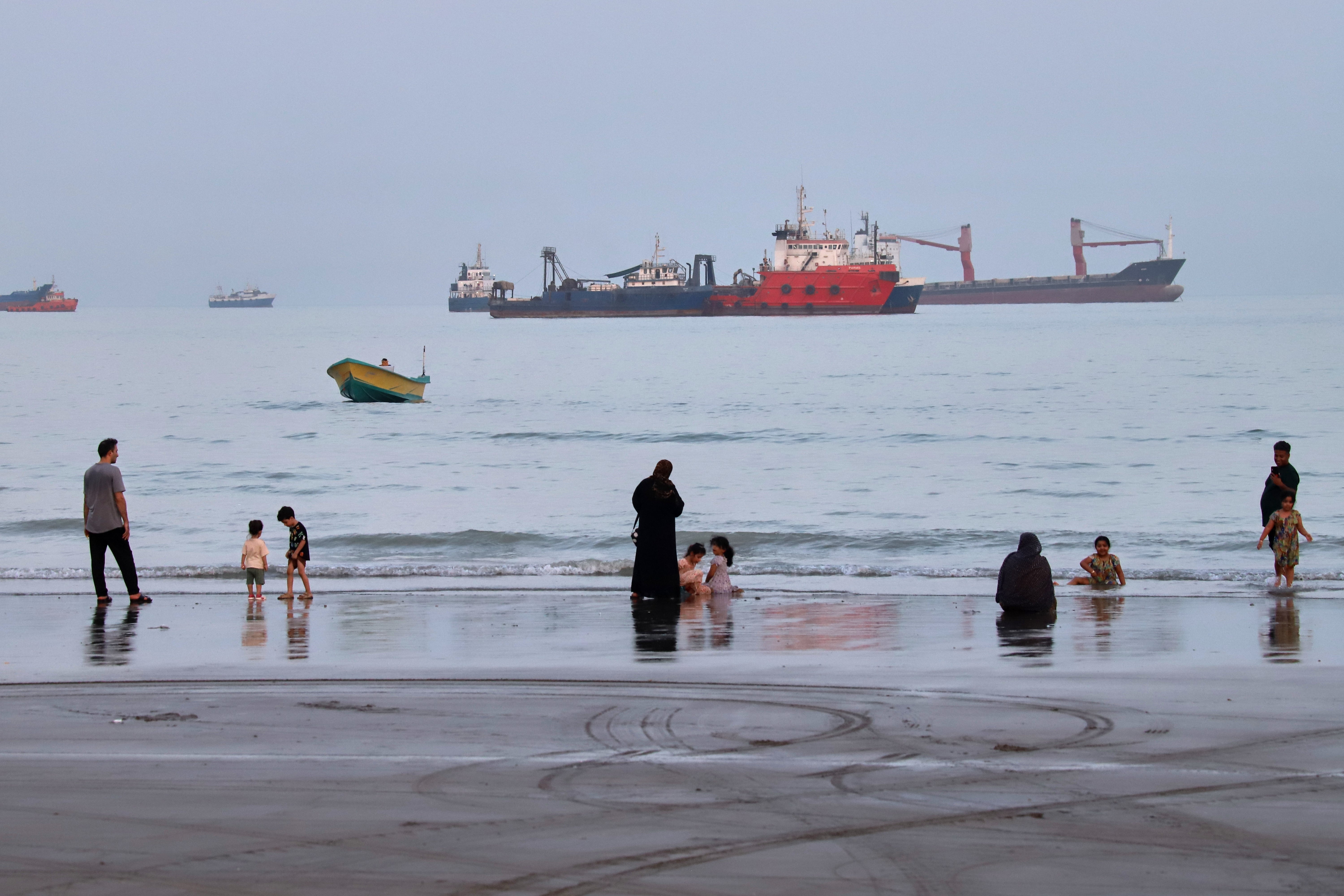 People spend time at a beach as commercial vessels are anchored in the Strait of Hormuz off Bandar Abbas, Iran, Wednesday, Aug. 5