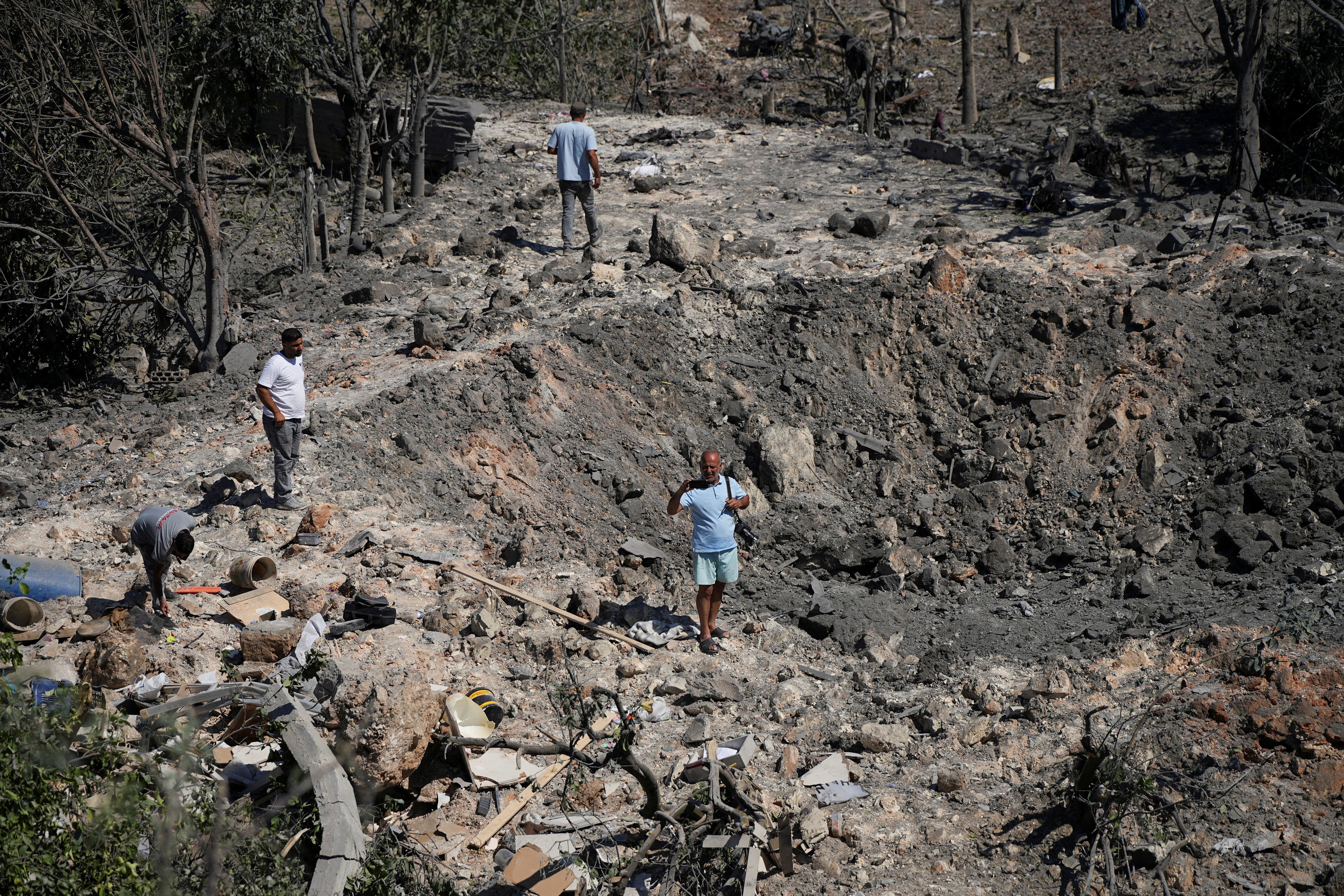 People and journalists stand at a site hit by Israeli strikes that occurred in the early hours of Thursday, according to Lebanon’s state news agency NNA, in Burj al-Shamali