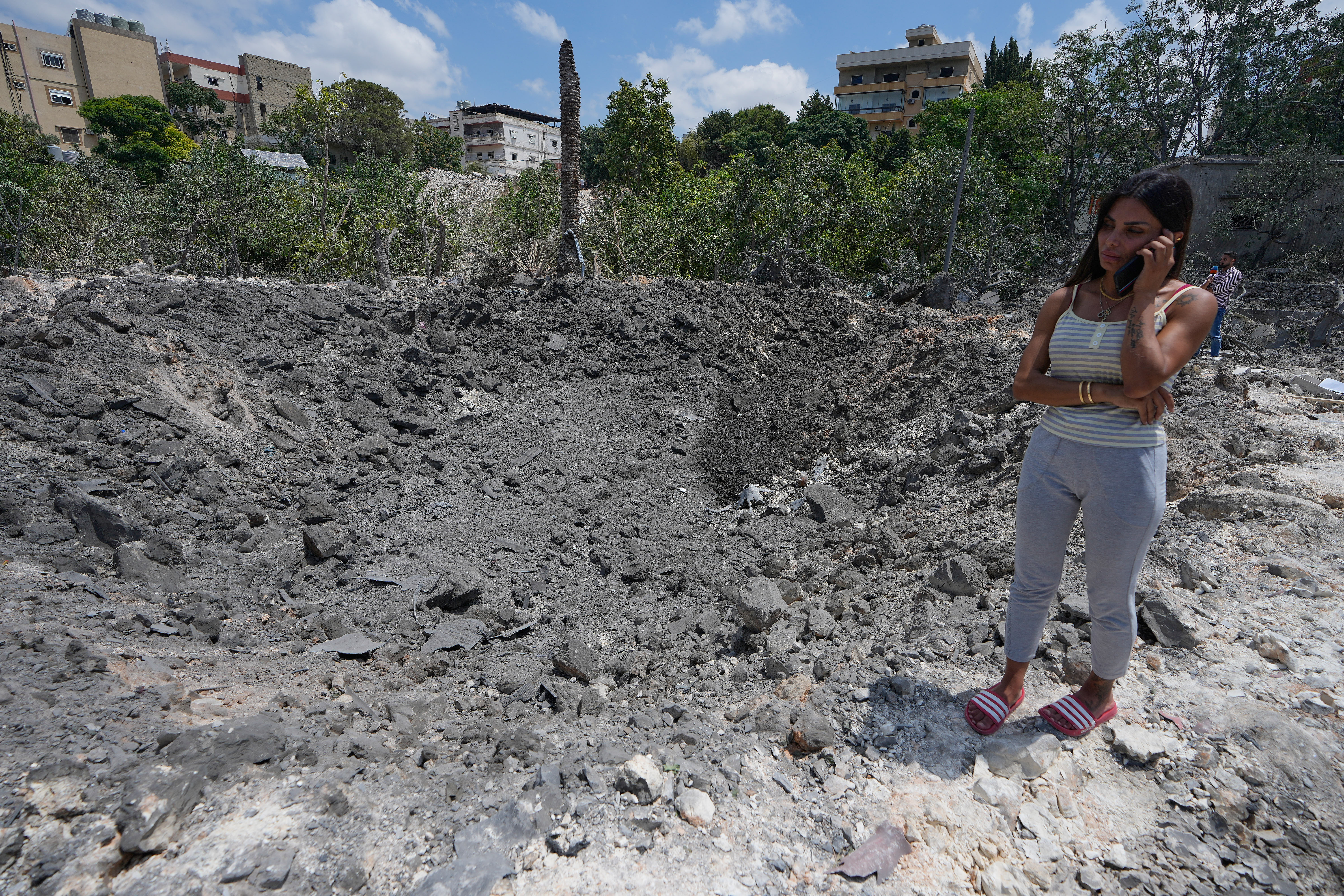 Hanan Jeha speaks on her phone next to a crater on a place of her family house, hit by an Israeli airstrike in Burj al-Shamali village, south Lebanon (AP)