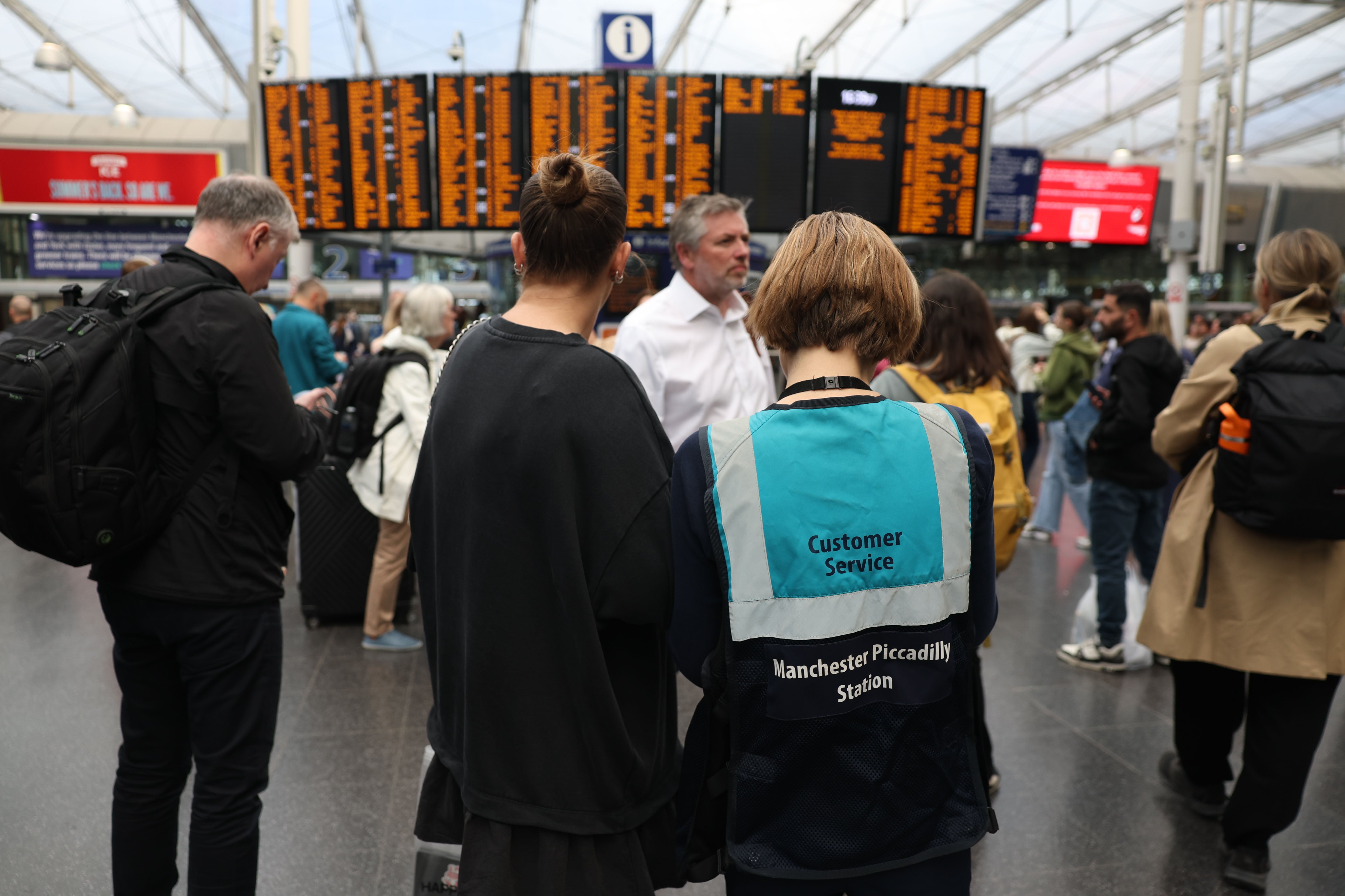Passengers stand with a customer service person inside Manchester Piccadilly train station after a major disruption to rail service in the Midlands and northwest England