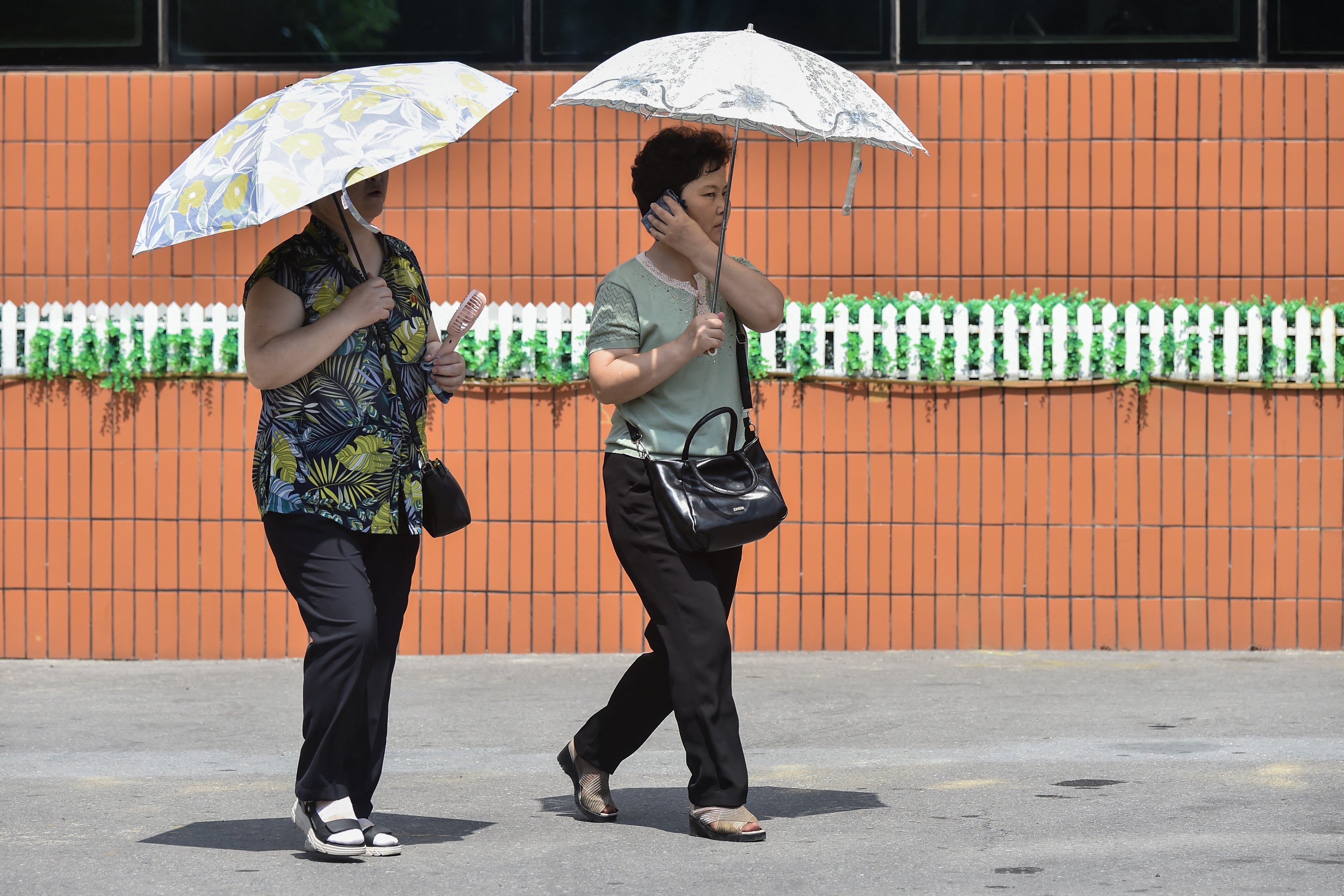 Women use umbrellas to shelter from the sun while walking along Mirae Scientists Street in Pyongyang on August 4, 2026