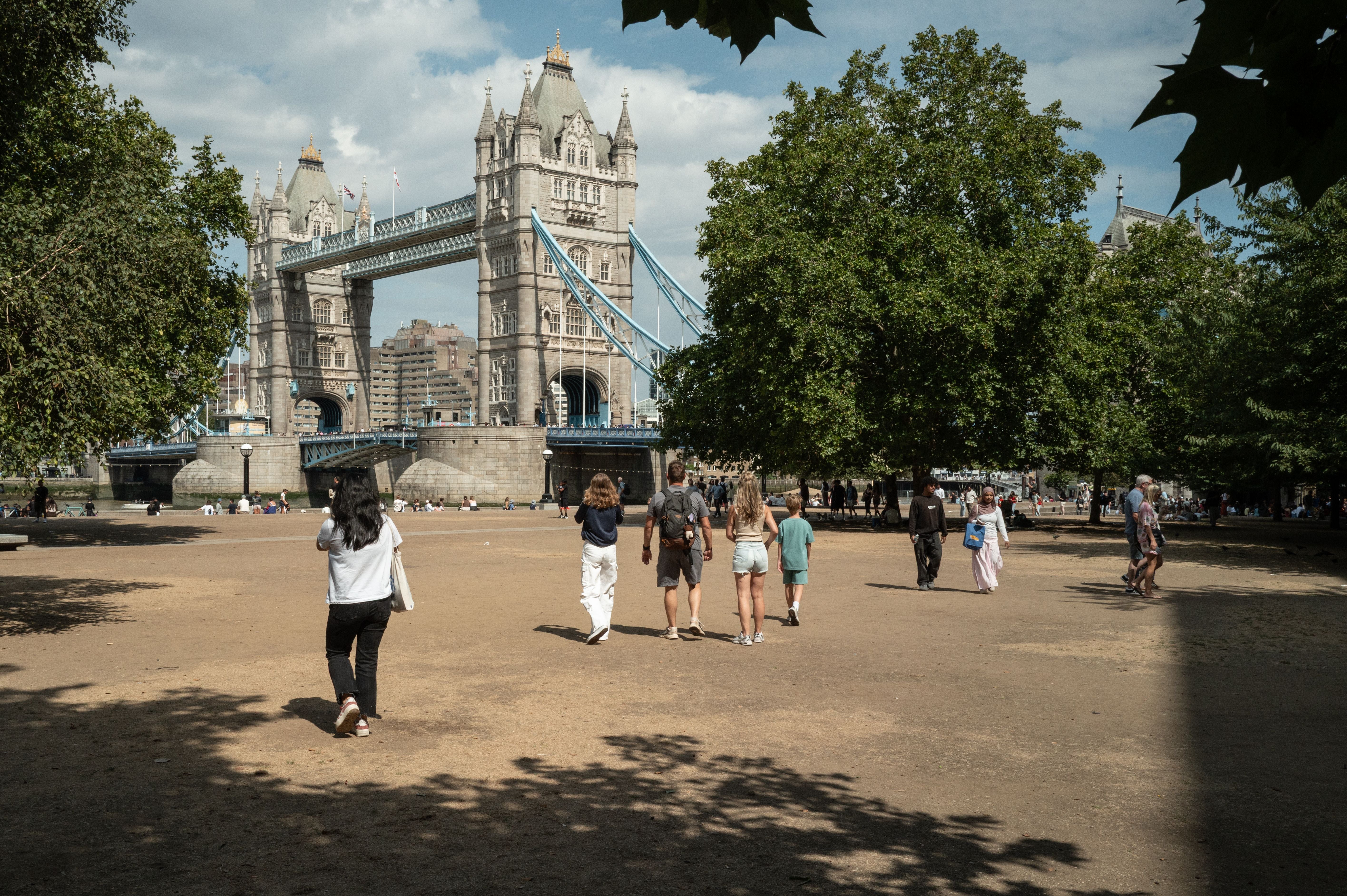 Tourists walk on the parched earth and sun-damaged grass near Tower Bridge on Sunday