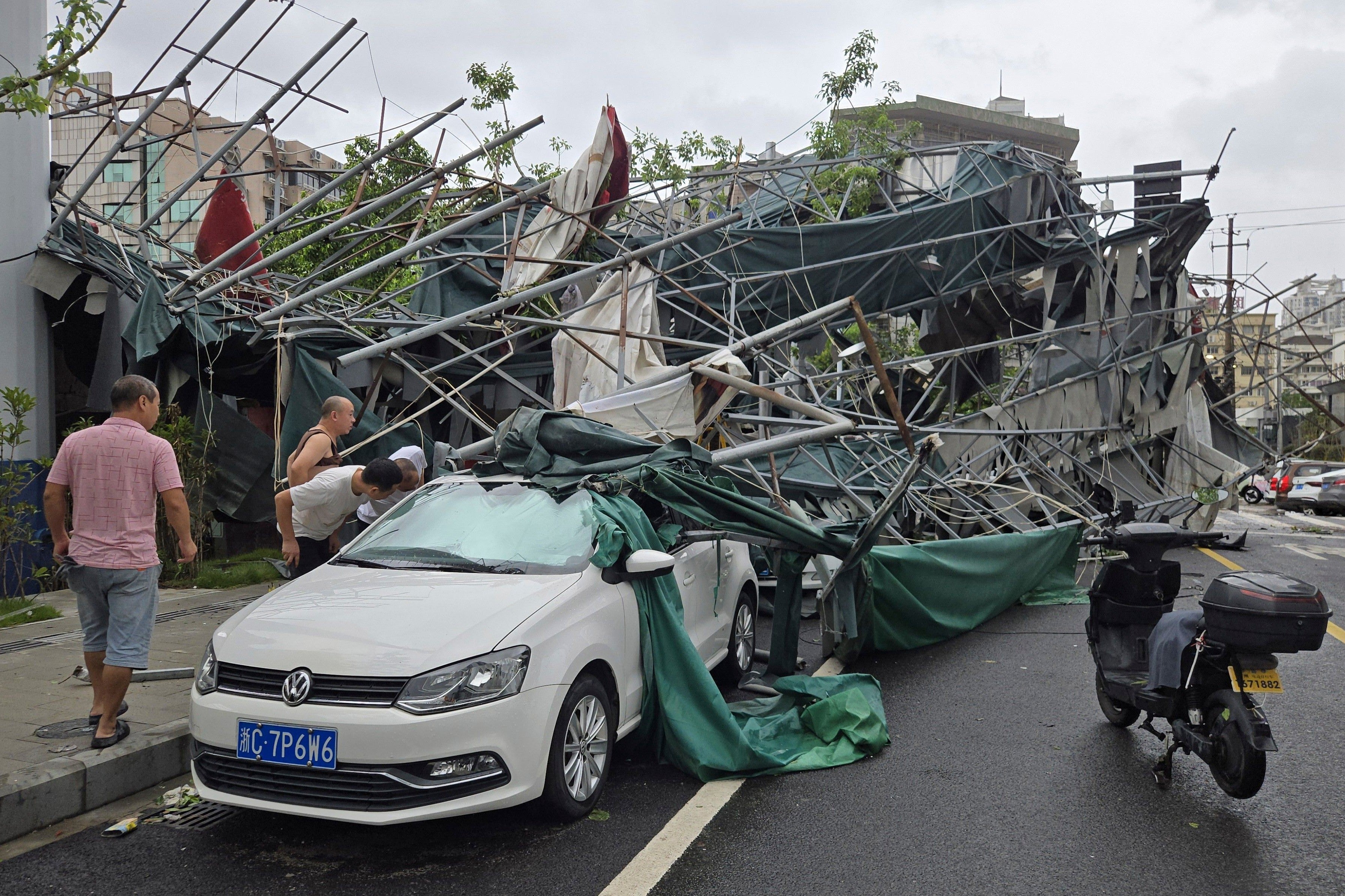 People look inside a car pinned by a fallen scaffolding structure after Typhoon Dolphin (AP)