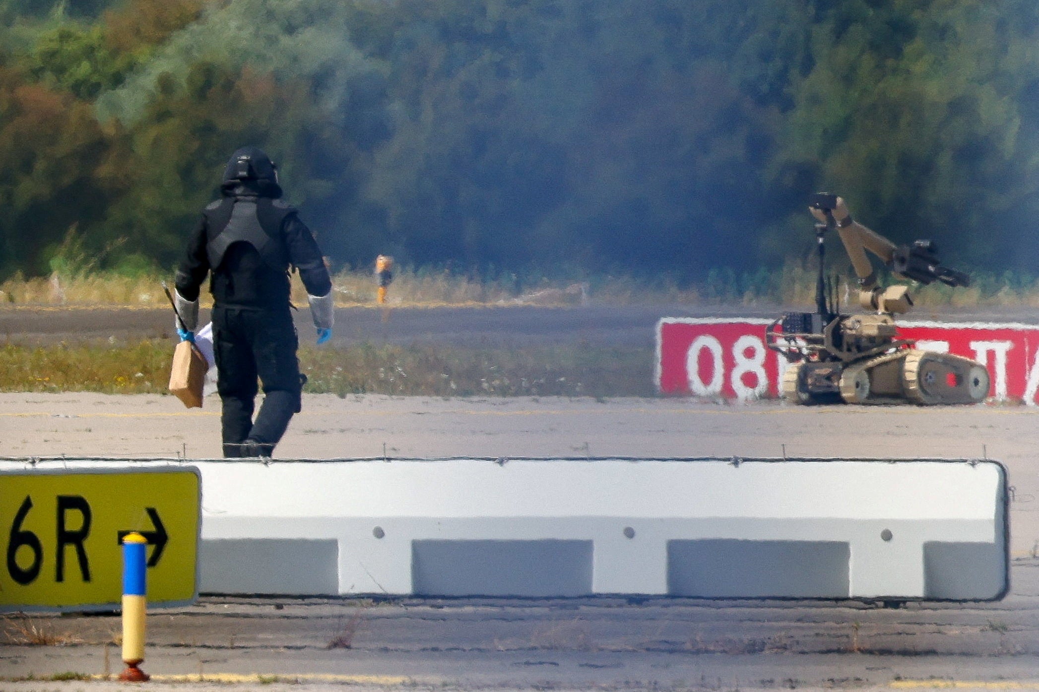 A police officer in protective clothing walks next to an explosive-disarming robot (EOD) at Leipzig/Halle Airport in Schkeuditz, Germany (Reuters)