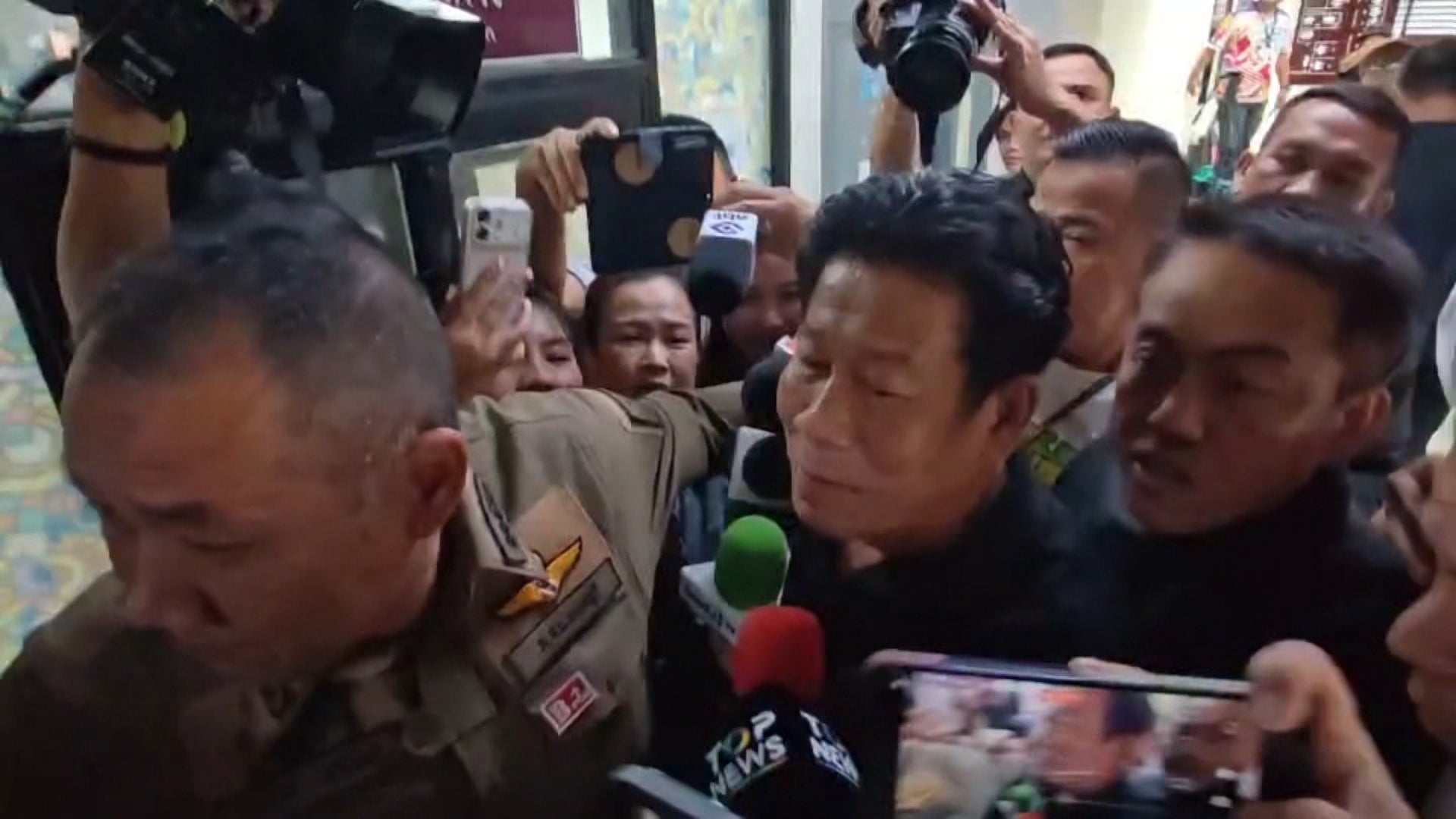 In this image made from video provided by the Thai Public Broadcasting Service, Chalong Riewraeng, center, former local Thai lawmaker, walks past media members in Nonthaburi (TPBS)
