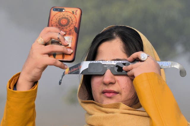 <p>Una mujer utiliza lentes con filtro solar mientras toma una foto de un eclipse solar con su teléfono inteligente en Islamabad, Pakistán, el 26 de diciembre de 2019</p>