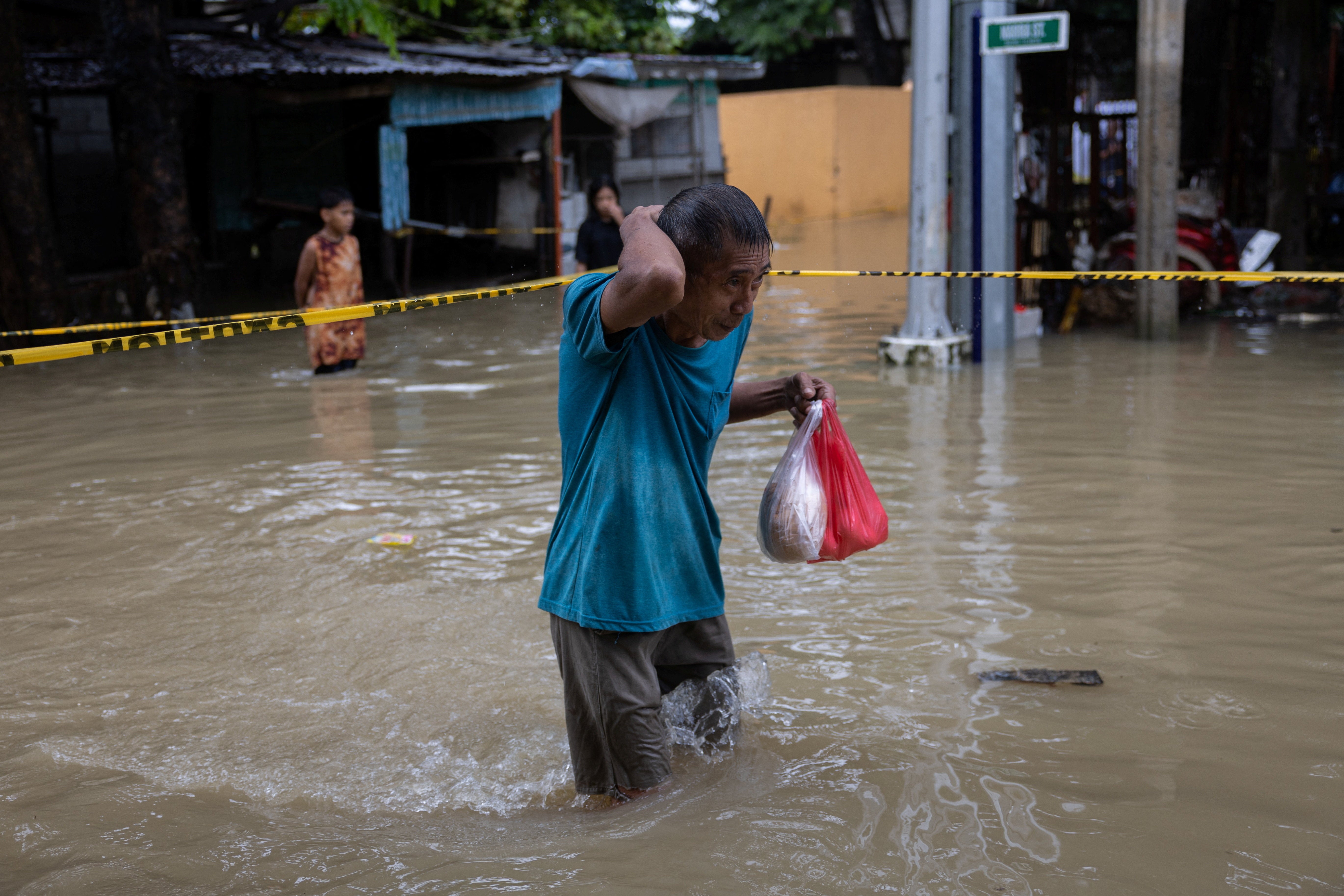 A man carrying plastic bags of food wades through floodwaters in Bagong Silangan, Quezon City, Philippines