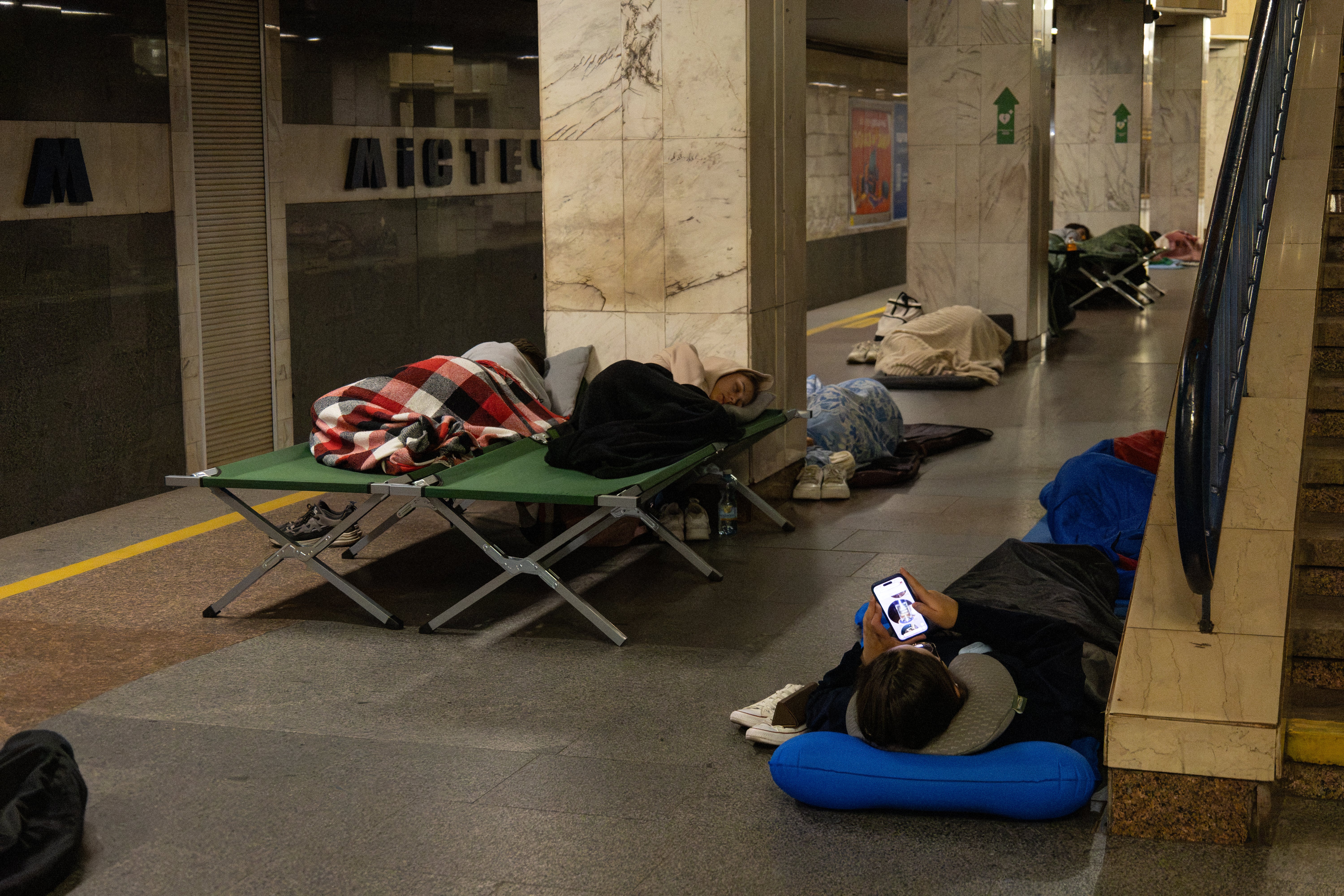 A person checks a smartphone and others sleep as they take shelter overnight in a Kyiv metro station, following warnings of a possible Russian air attac