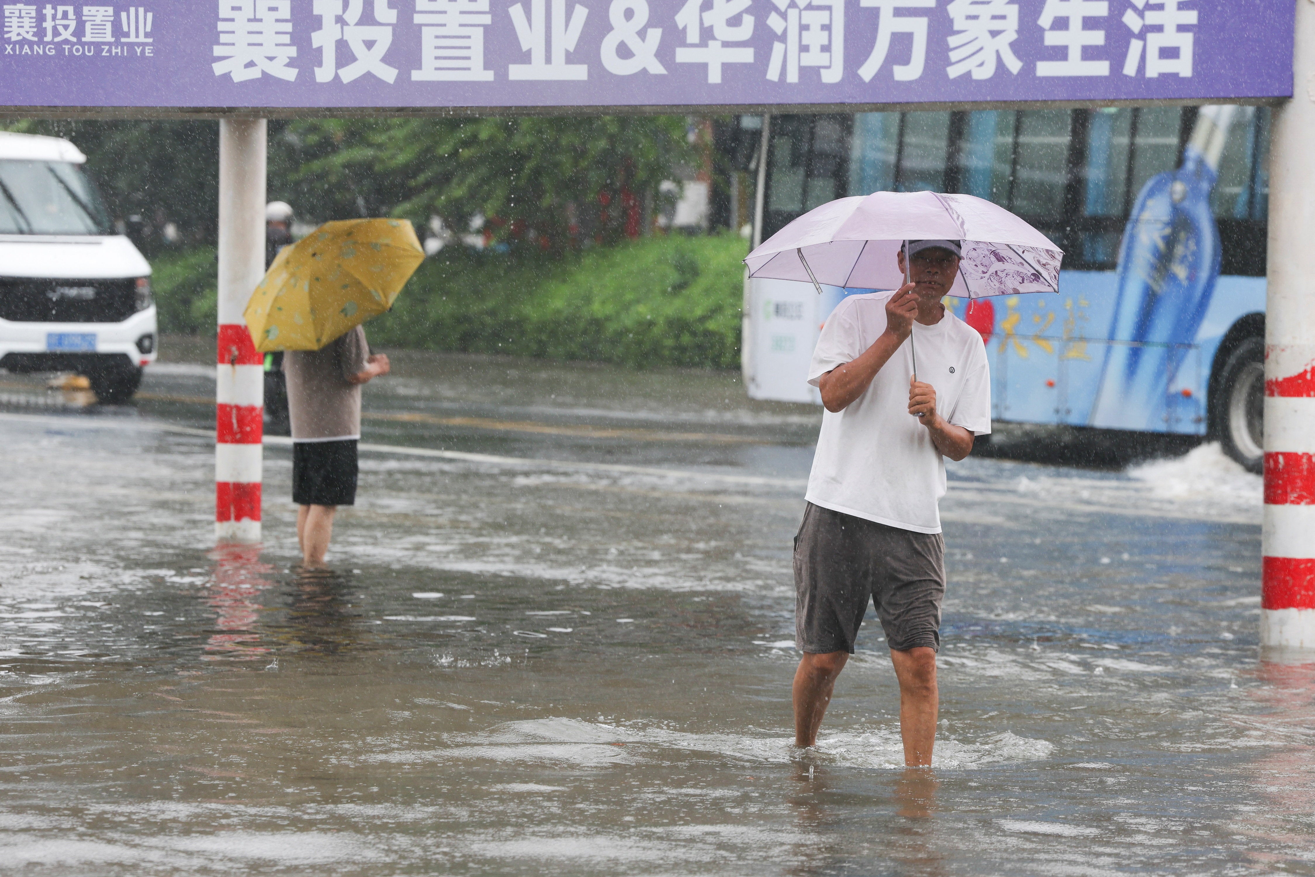People walk through a flooded street during heavy rain brought by Typhoon Dolphin after it weakened into a tropical storm, in Xiangyang, Hubei province, China, August 11, 2026