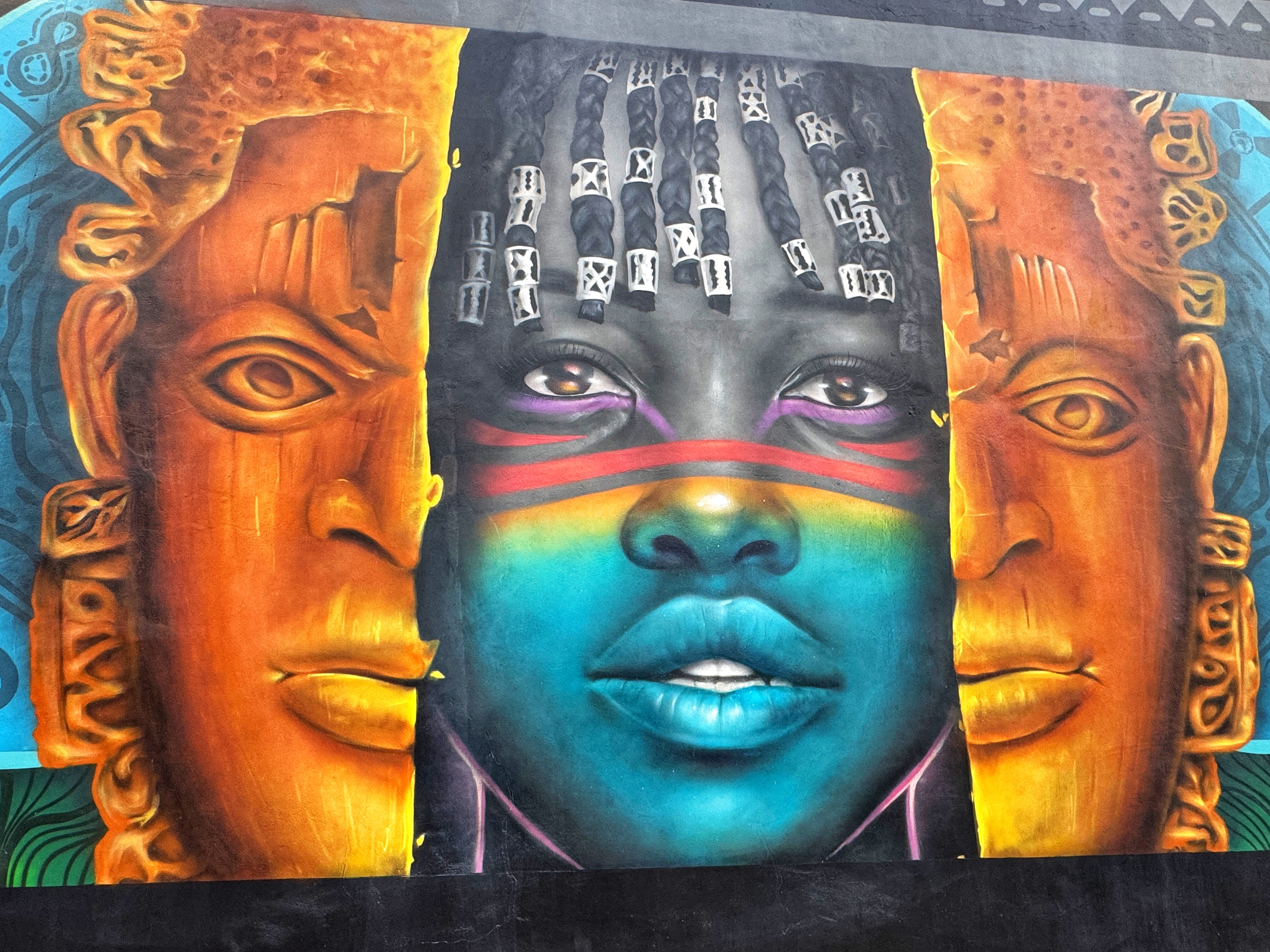 A mural shows an ancient mask splitting open to reveal a teenage girl at Marina Boulev’art