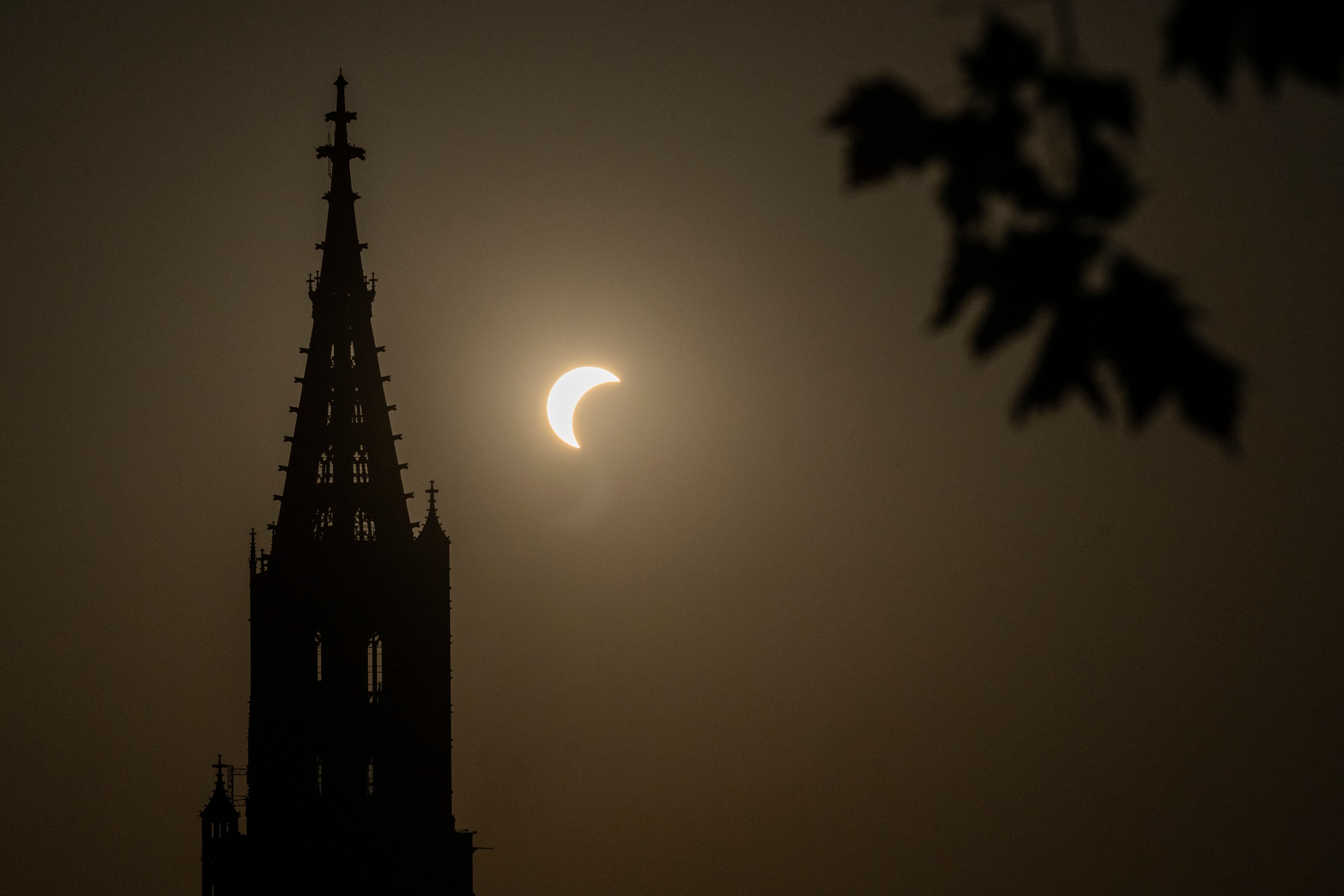 The moon obscures the sun during a partial solar eclipse seen next to the Cathedral in Bern, Switzerland (AP)