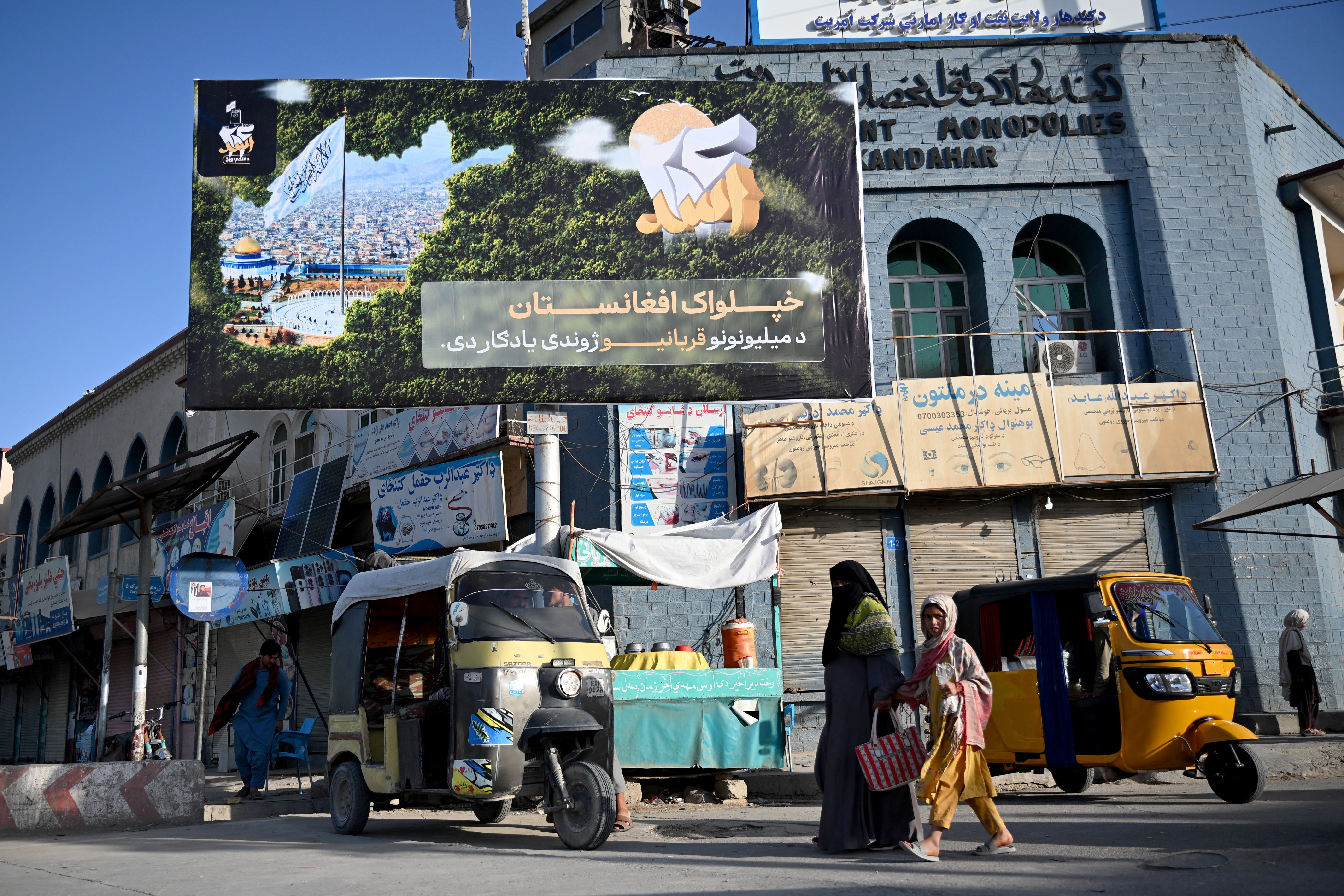 Afghans walk past a board displaying slogans by the Taliban administration in Kandahar