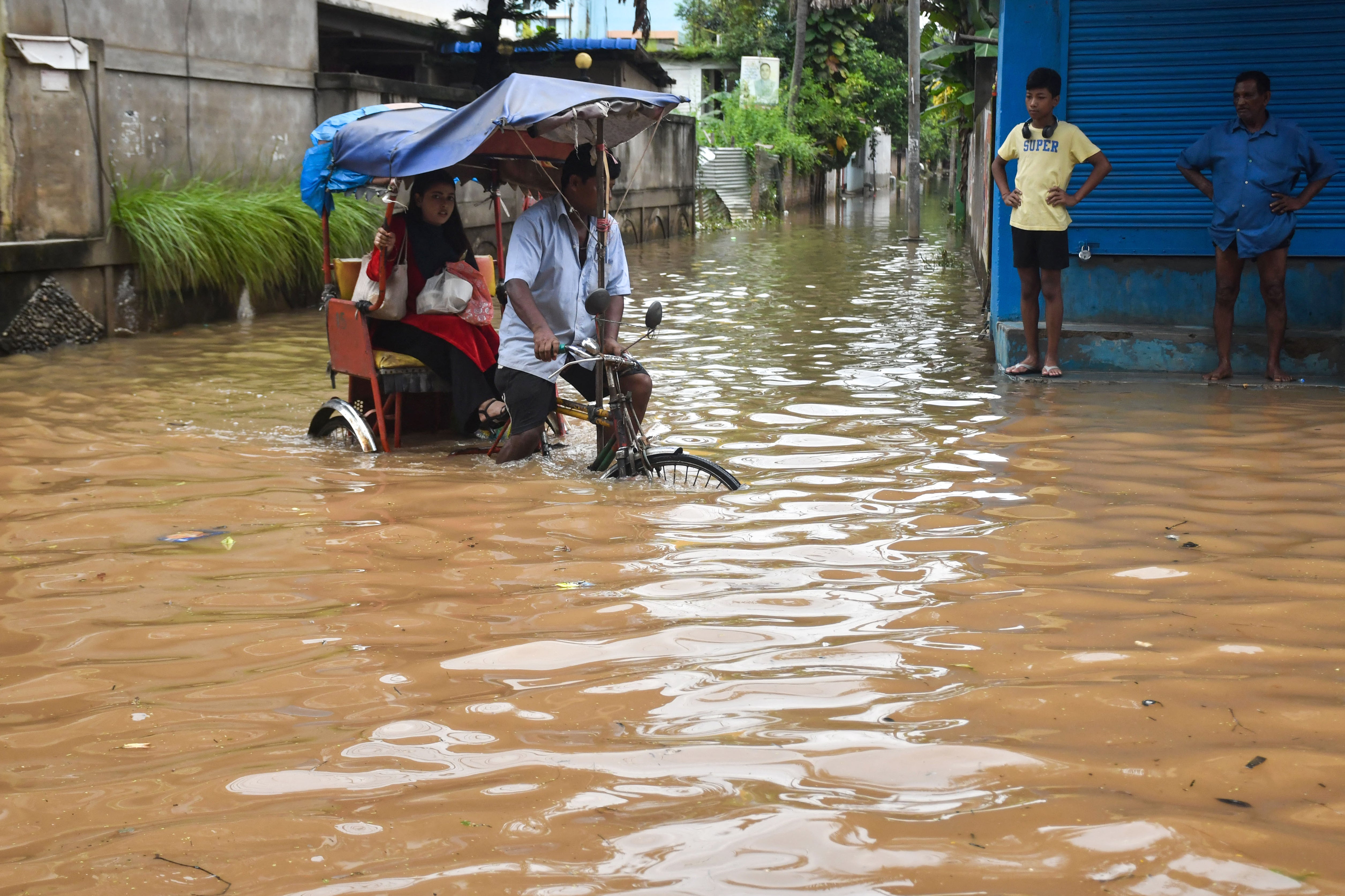 A resident commutes in a cycle rickshaw through a flooded street following heavy rainfall in Guwahati, Assam
