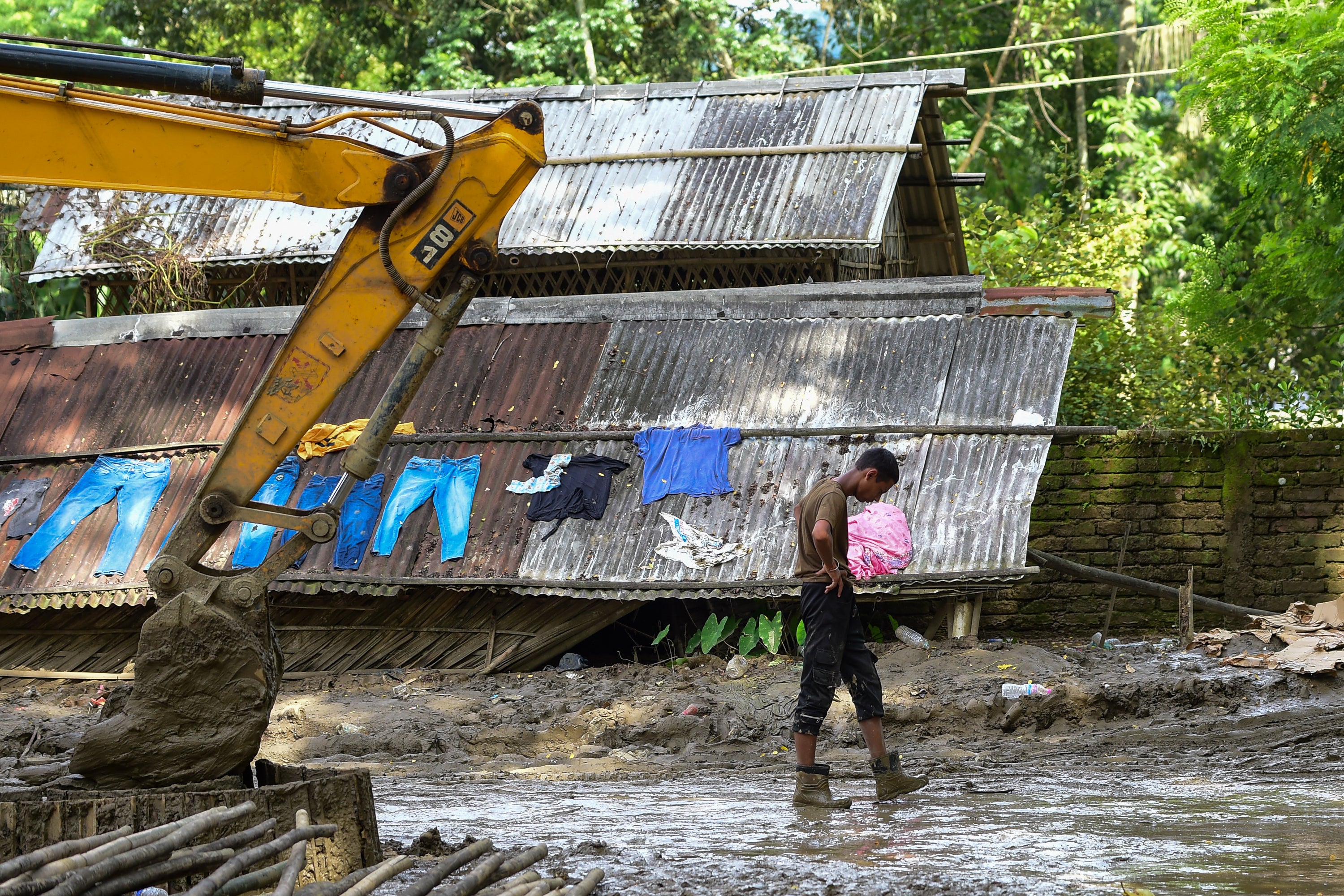 A resident walks past an excavator clearing mud and debris beside a flood damaged house