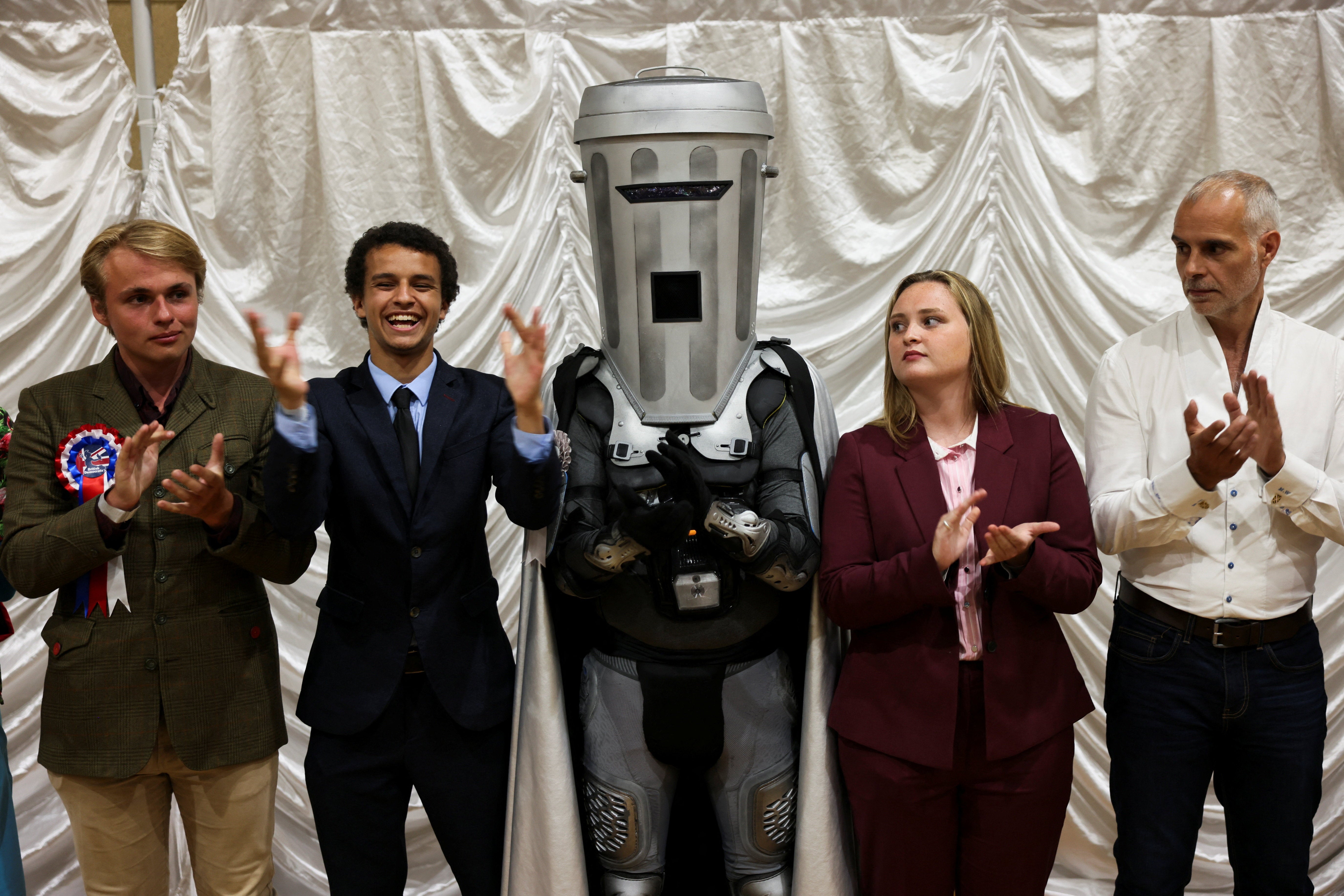 Count Binface gestures while standing with other candidates after Reform UK party leader Nigel Farage was declared the winner for the Clacton by-election, triggered by the resignation of Farage, in Essex, Britain, 14 August 2026