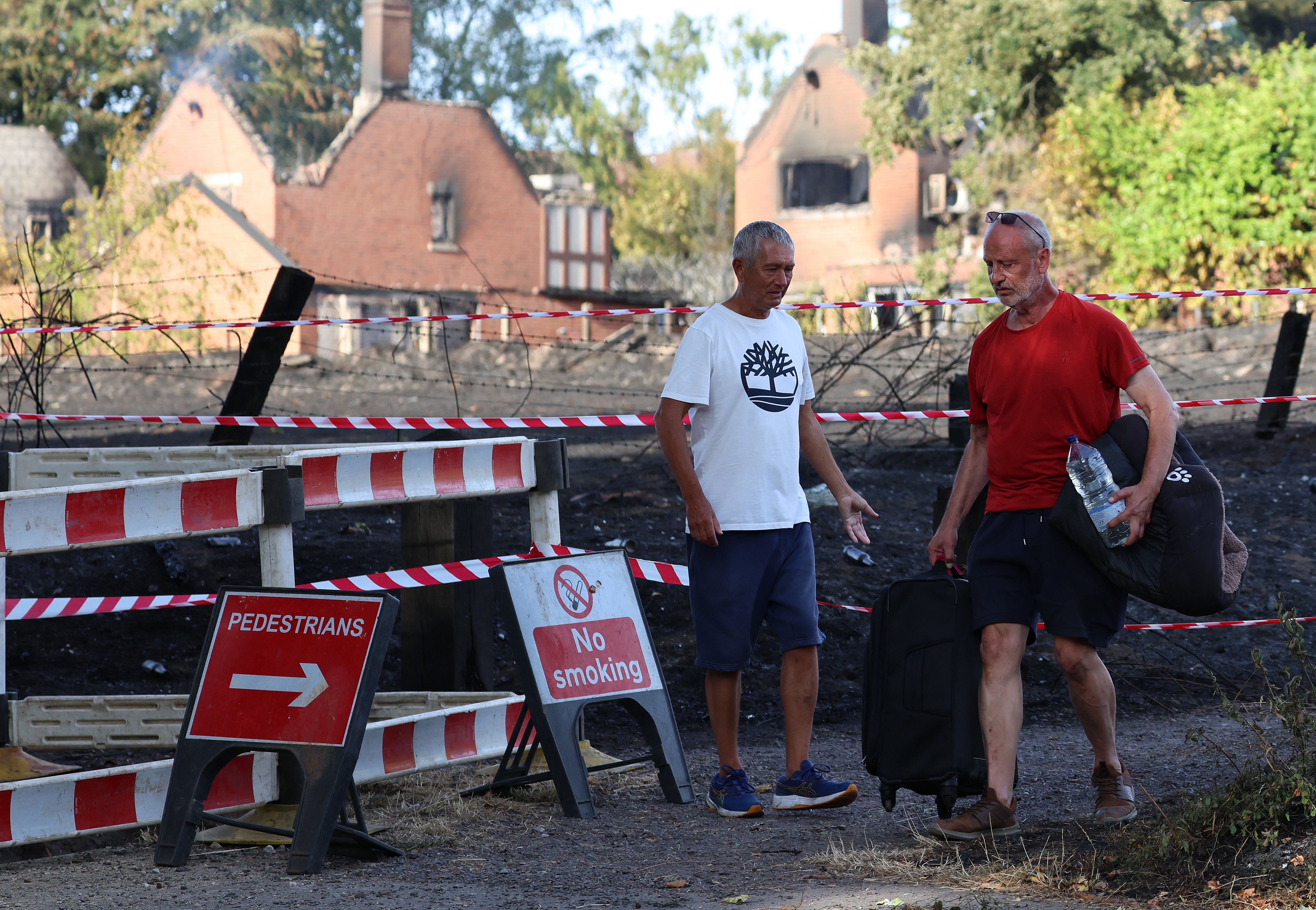 A person carries belongings in a suitcase, and a dog bed under their arm, as they walk near fire-damaged houses after a series of wildfires, in Stourbridge (AFP/Getty)