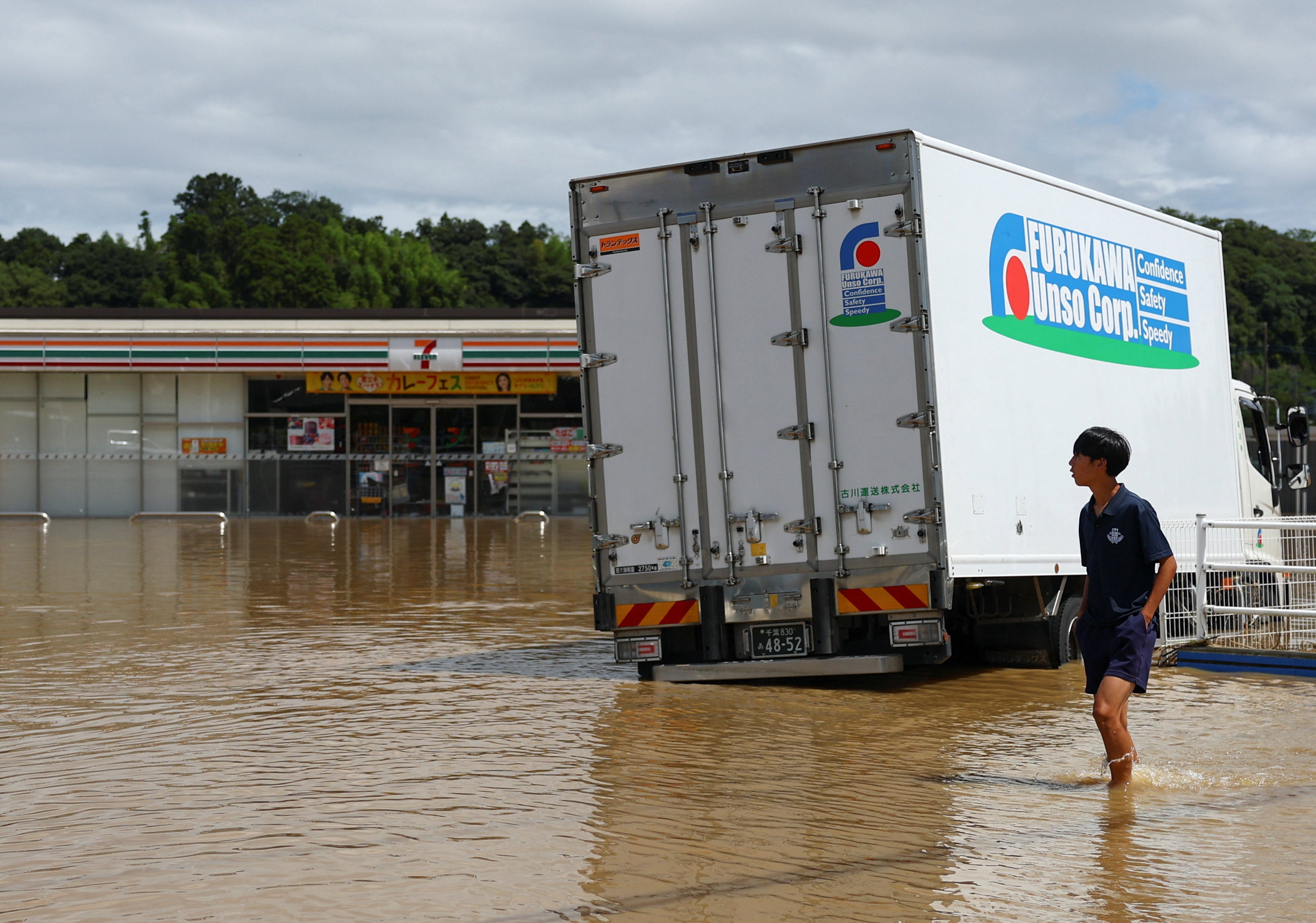 A resident walks near a 7-Eleven store in a flooded area after heavy rain in Oamishirasato, Chiba (Reuters)