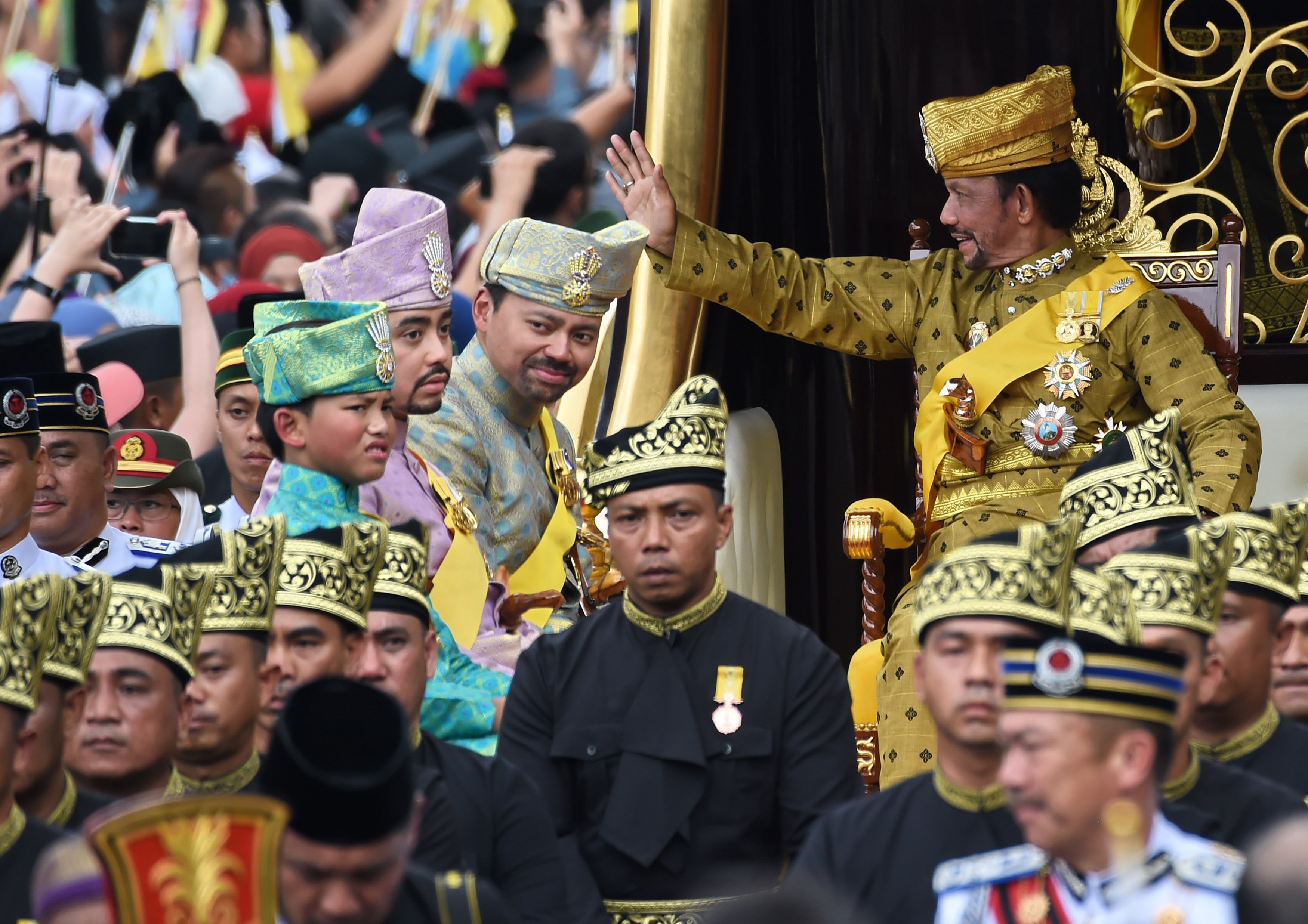 Sultan Hassanal Bolkiah waves while Crown Prince Al-Muhtadee Billah, second right, Prince Abdul Malik, second left, and Prince Abdul Wakeel, left, look on from the royal chariot during a procession to mark his golden jubilee of accession to the throne in Bandar Seri Begawan on 5 October 2017 (AFP/Getty)